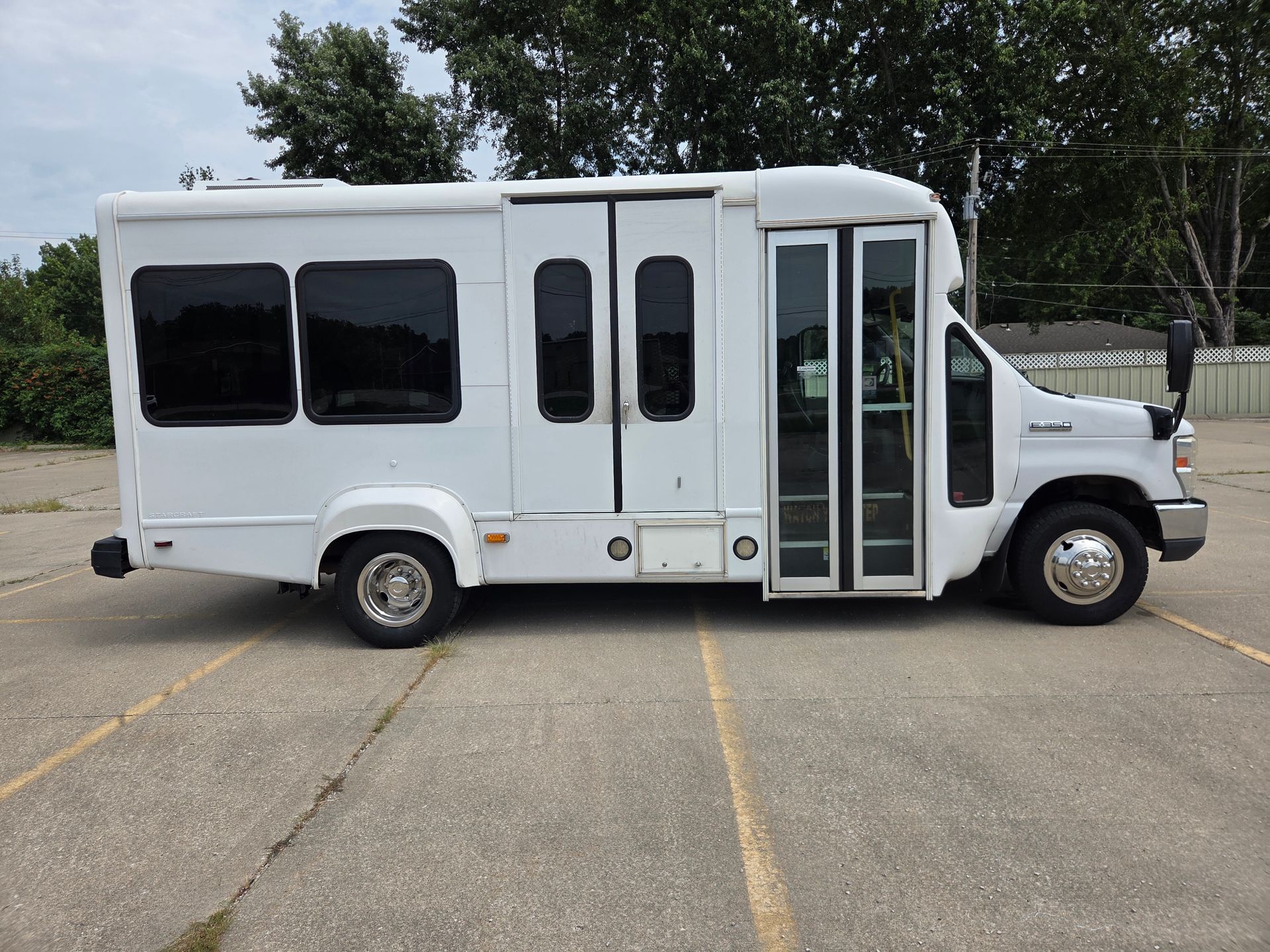 White shuttle bus parked in a lot, side view with windows and open front door