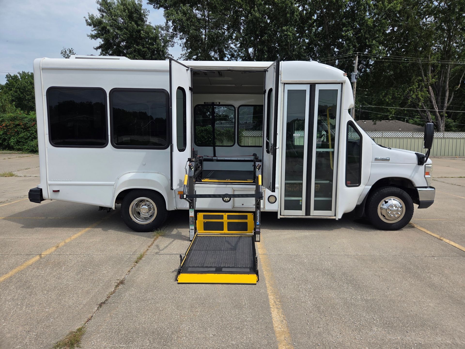 White shuttle bus with wheelchair ramp deployed, parked on pavement outdoors.