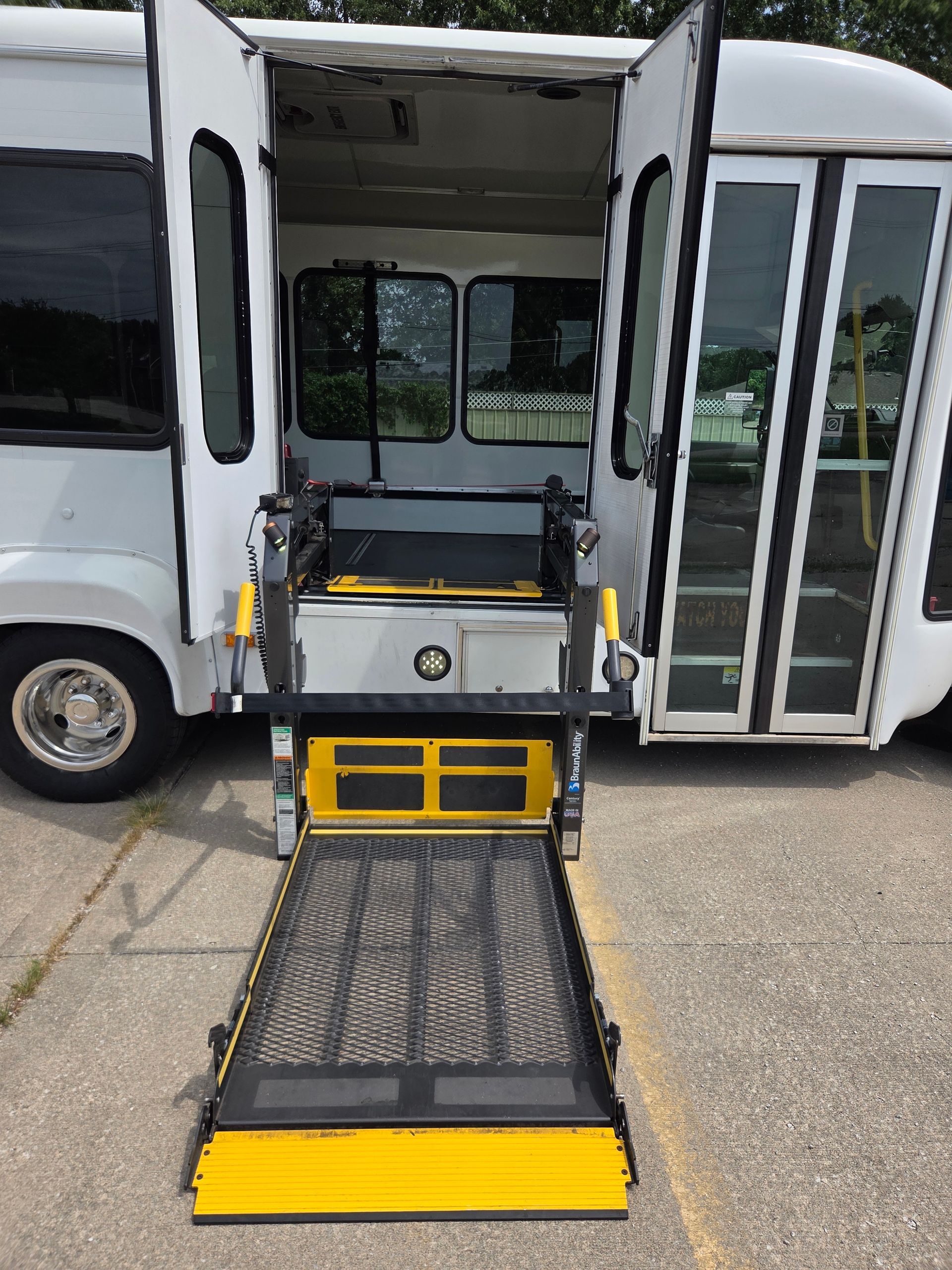 Open white shuttle bus with deployed wheelchair lift and yellow safety edges at the side door