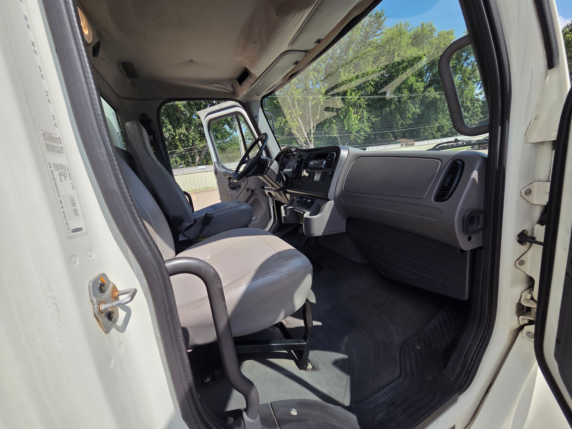 Empty van interior with gray seats, dashboard, and open side door in daylight