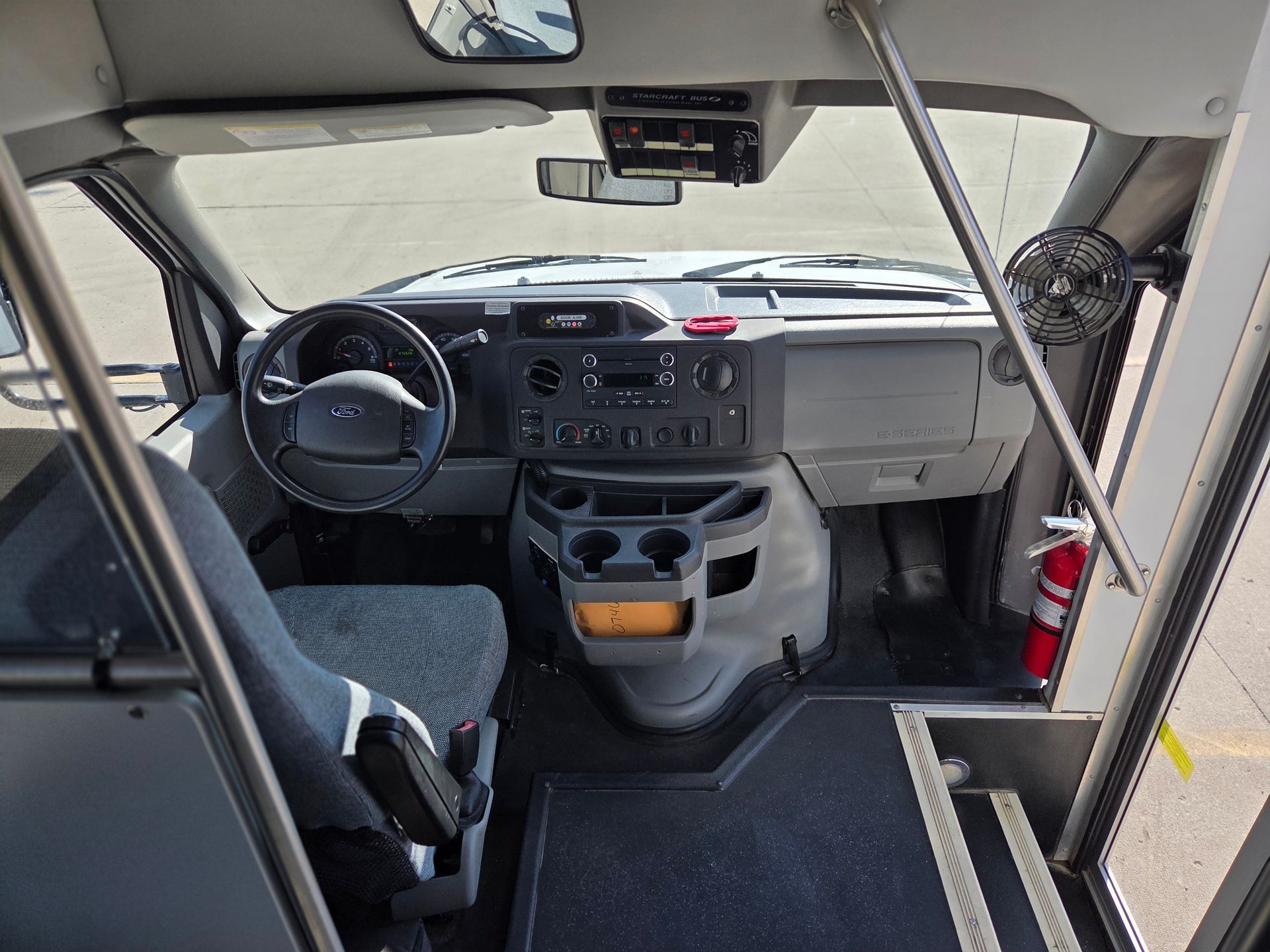 Interior of a vehicle cabin with steering wheel, dashboard, seats, and a fire extinguisher near the passenger side.