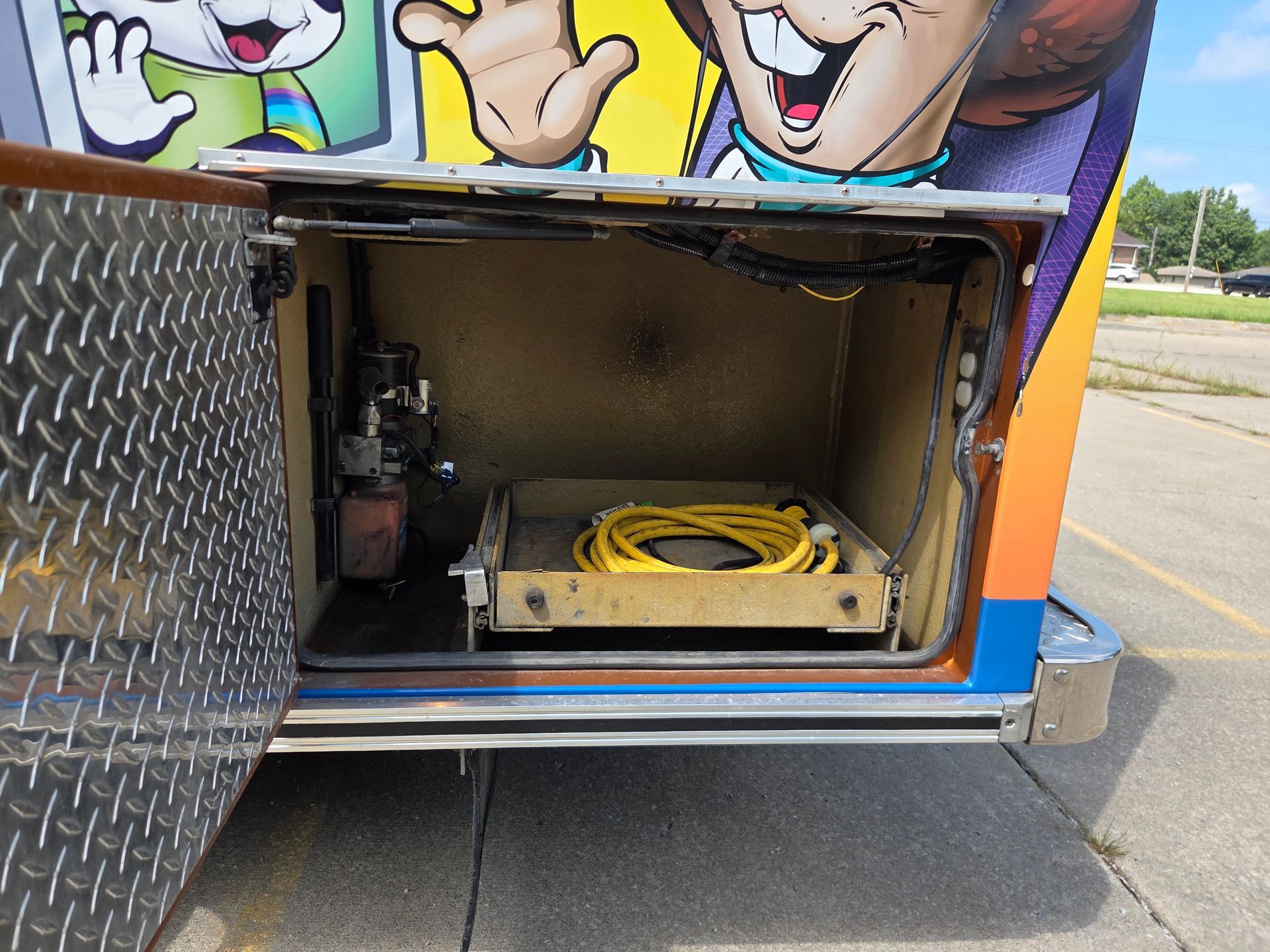 Open side compartment on a truck with coiled yellow hose and metal equipment inside