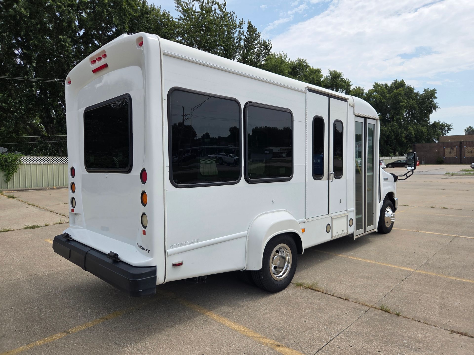 White shuttle bus with tinted windows parked in a lot under a partly cloudy sky