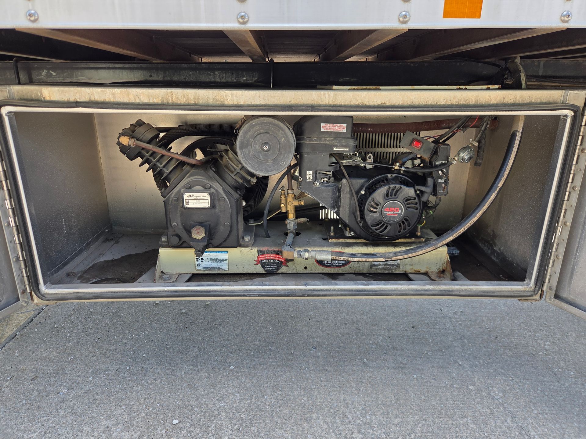 Engine compartment with a small air compressor mounted inside a metal utility vehicle bay.