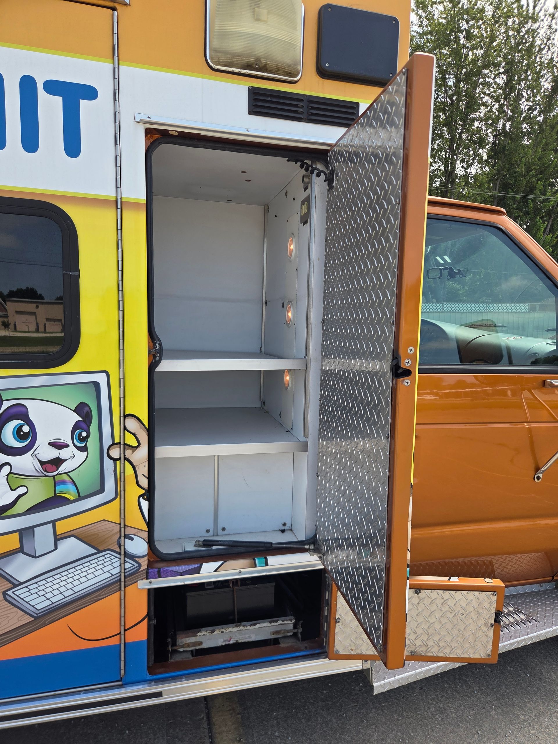 Open side door of orange-and-yellow food truck, showing empty white shelves inside.