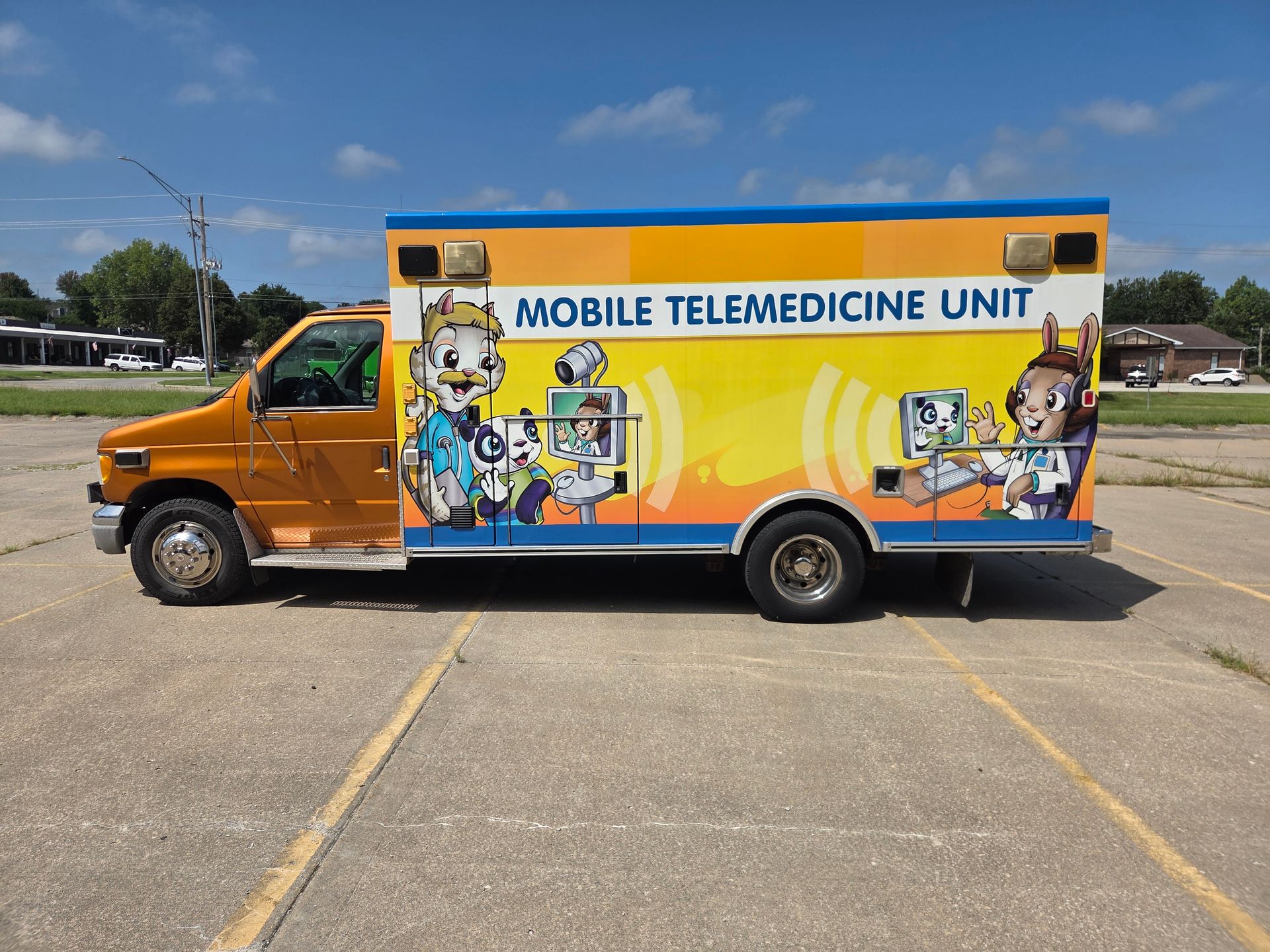 Orange mobile telemedicine unit van parked in a lot under a blue sky, with medical-themed graphics on the side.
