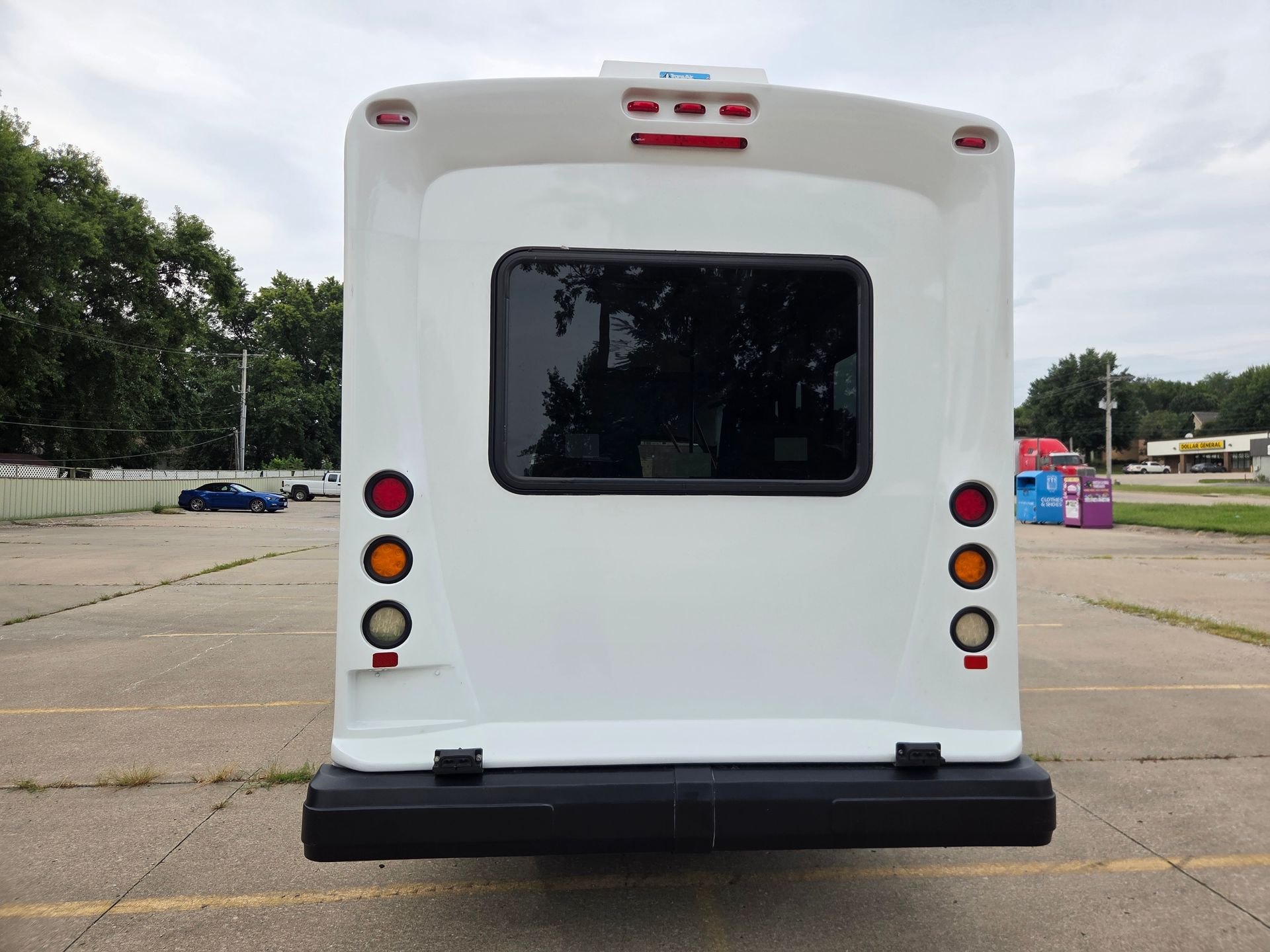 Rear view of a white shuttle bus with tinted window and red taillights in a parking lot