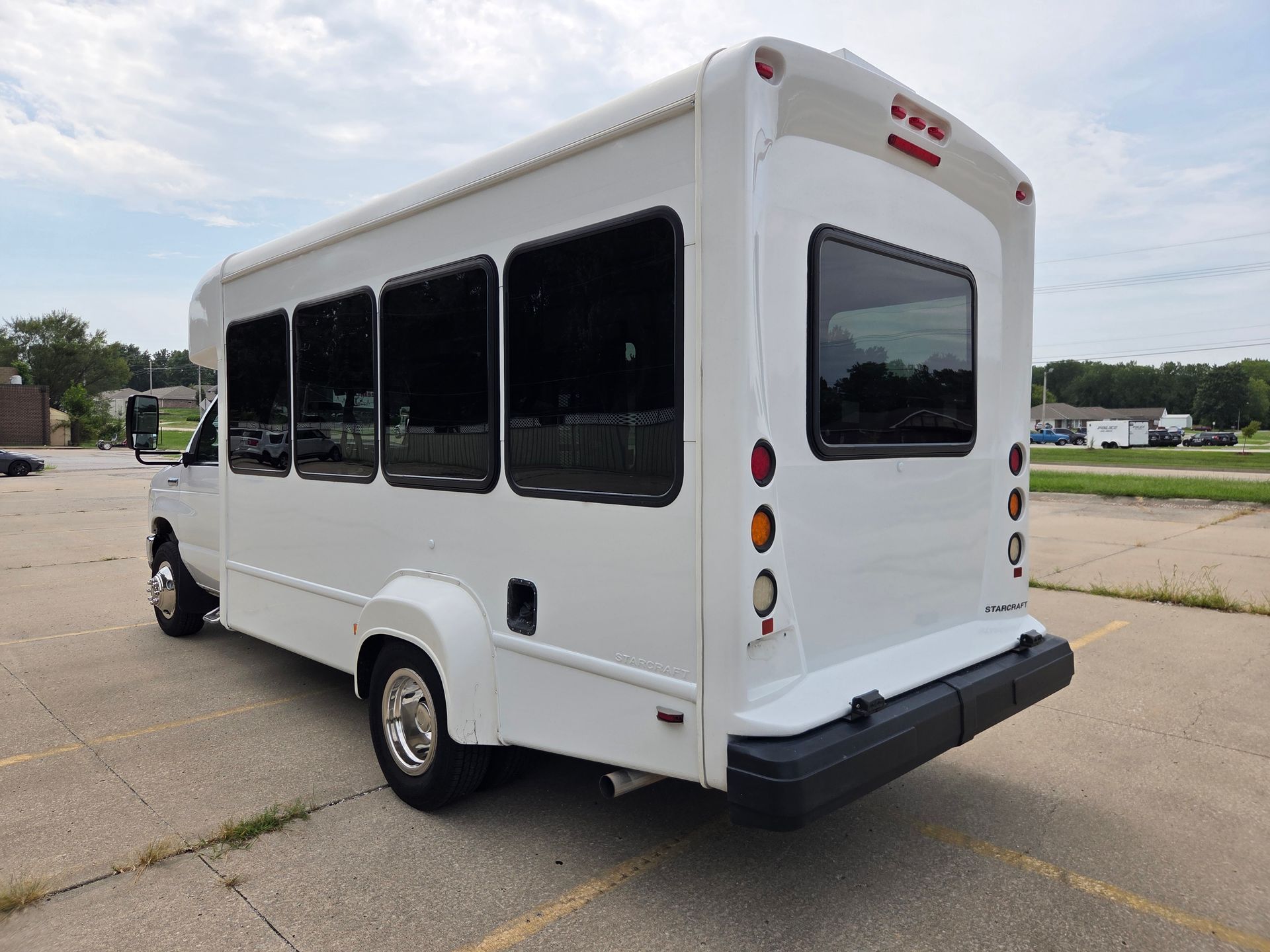 White shuttle bus parked on a paved lot under a cloudy sky, rear three-quarter view.