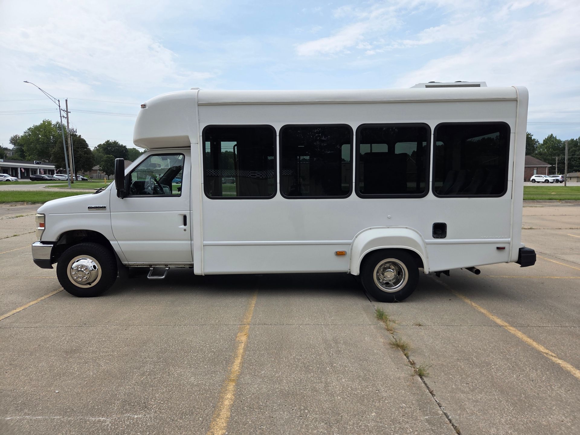 White shuttle bus parked in an empty lot, side view with tinted windows.