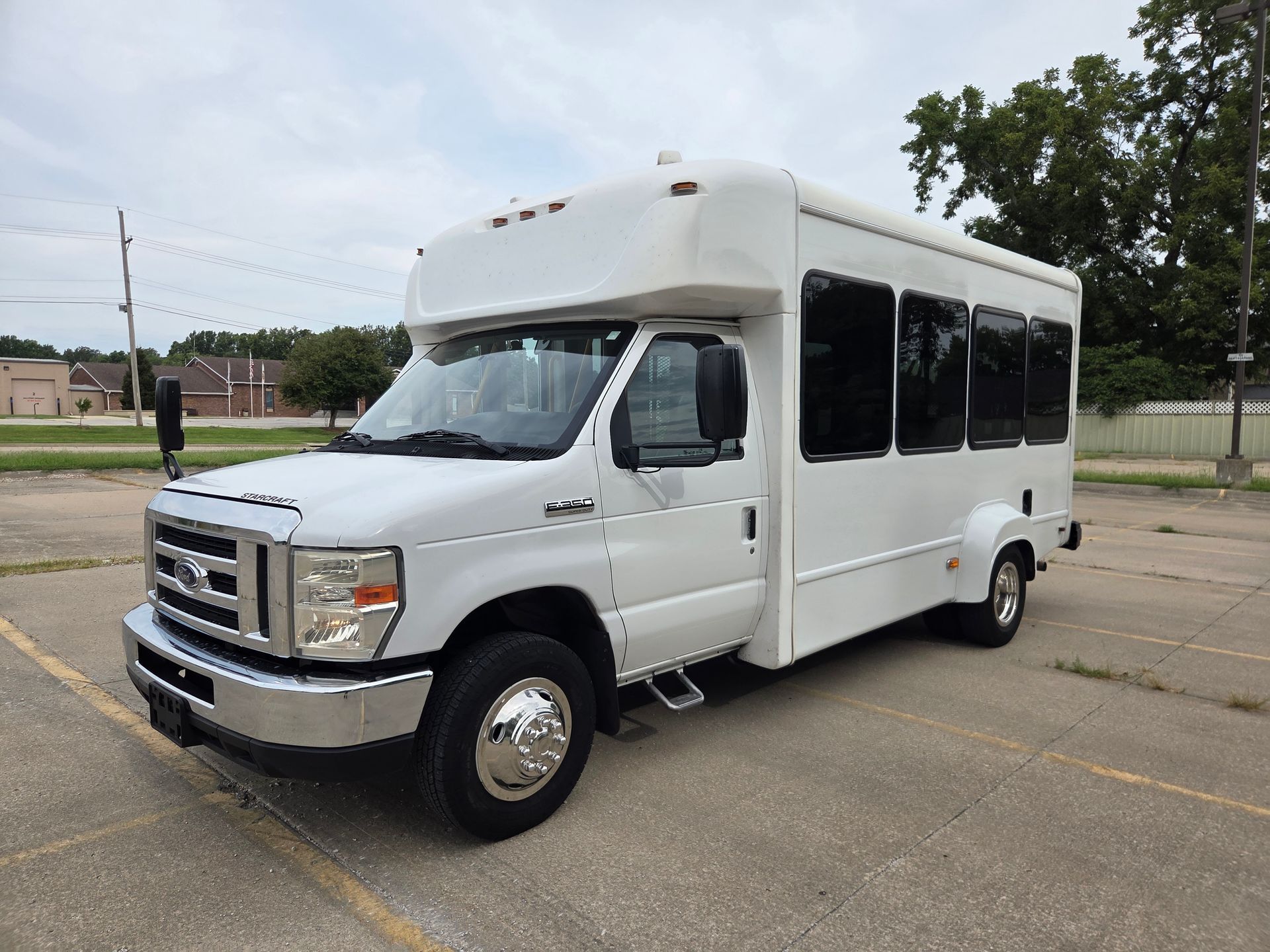 White shuttle bus parked on a lot under a cloudy sky.