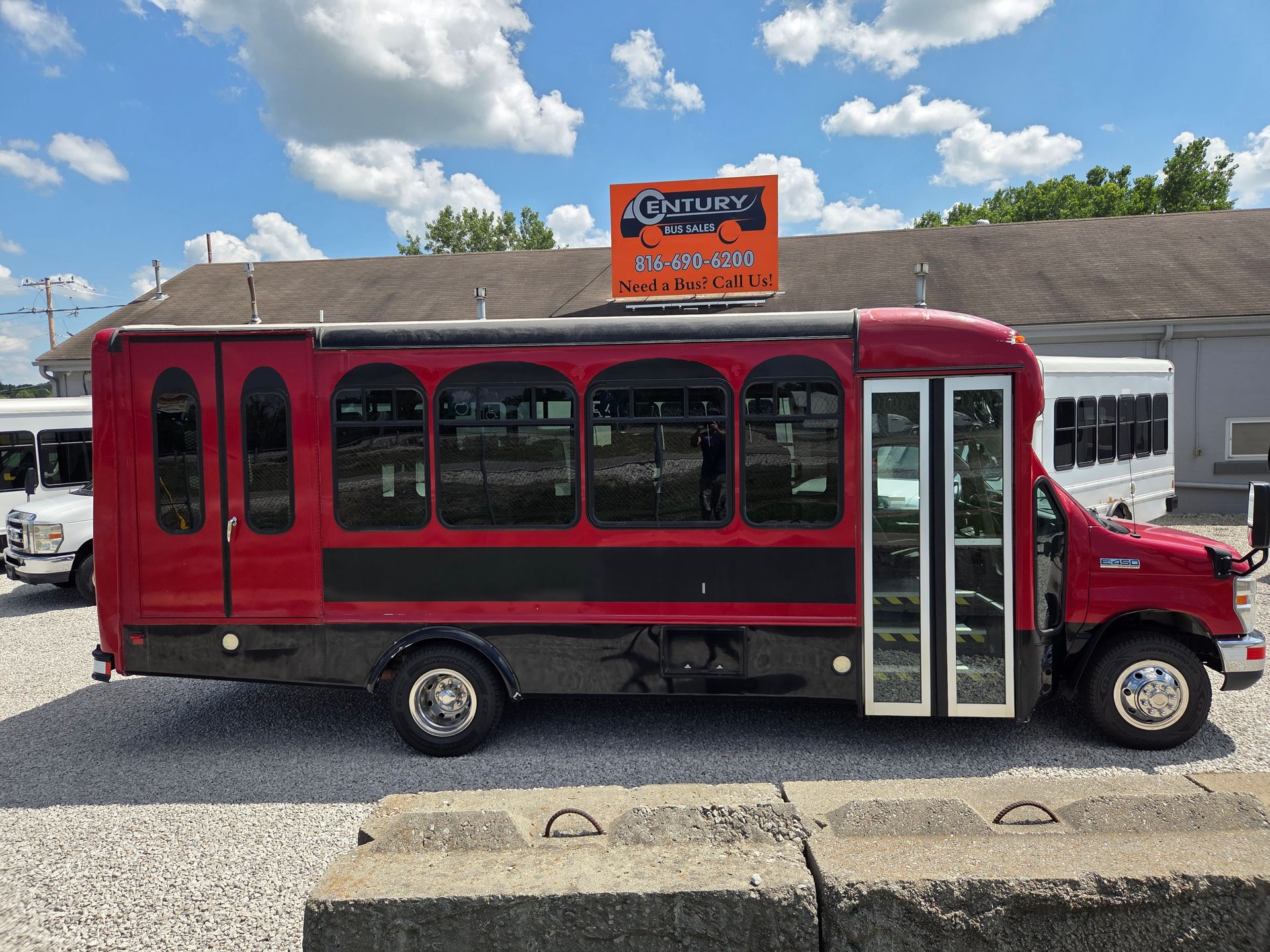 Red trolley-style shuttle bus with maroon canopy parked outside a building on a sunny day