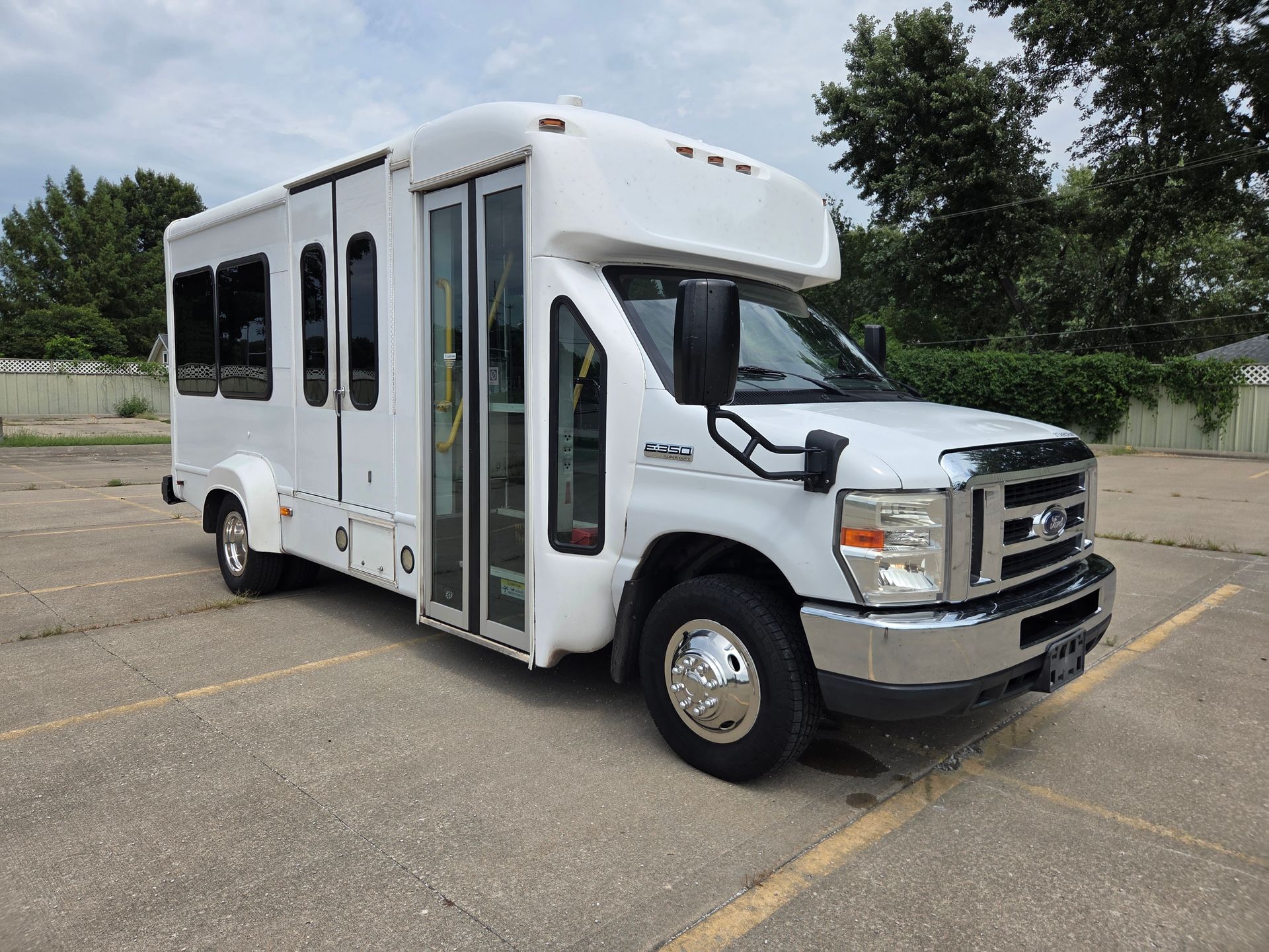 White shuttle bus parked in a lot, angled front view with tinted windows and an open side door