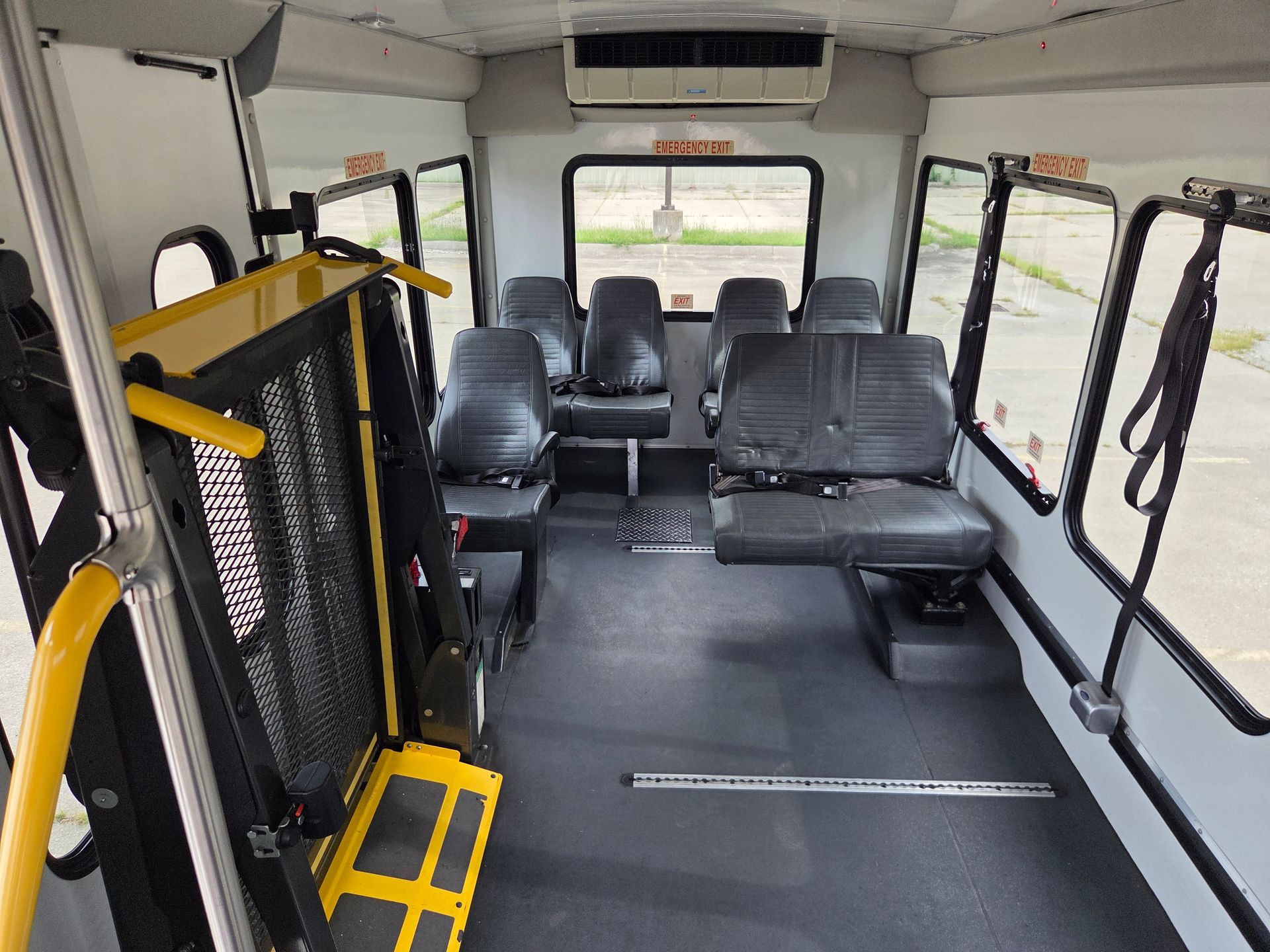 Interior of an accessible shuttle bus with black seats and a yellow wheelchair lift