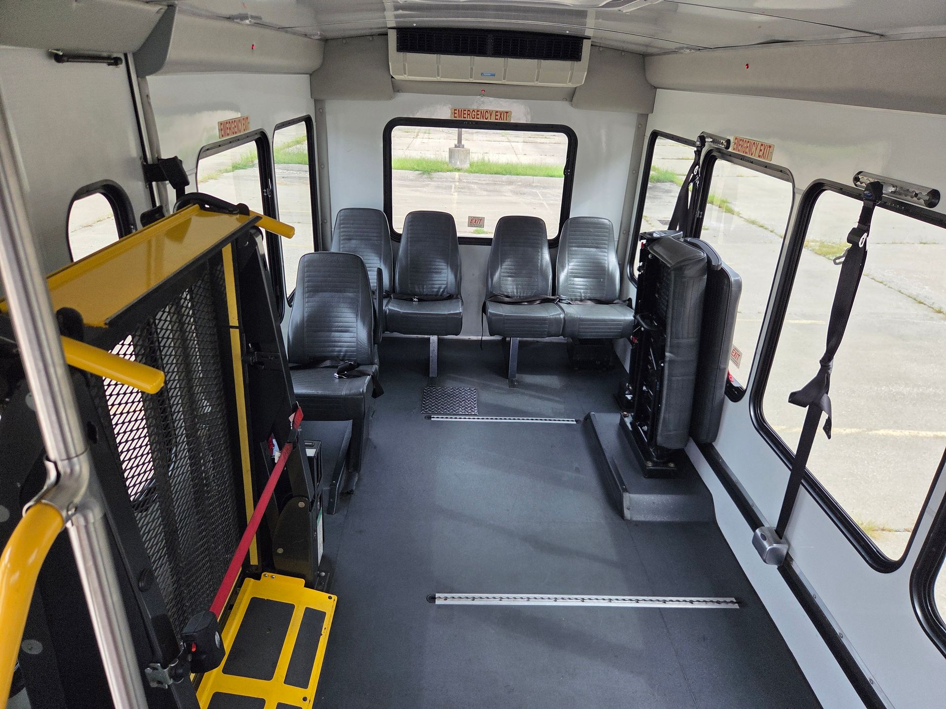 Empty shuttle bus interior with black seats and wheelchair lift equipment near the front.