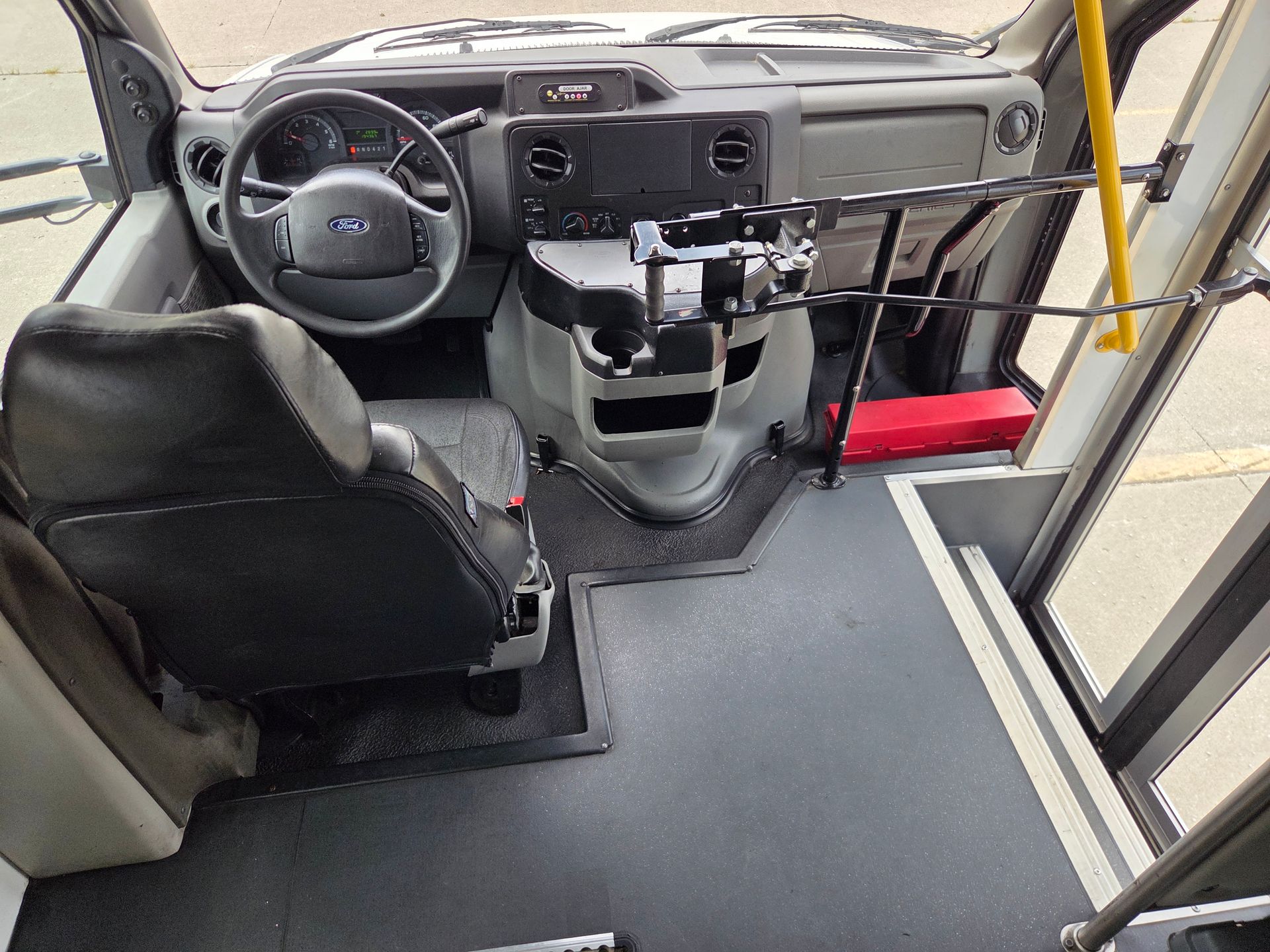 Bus driver area with steering wheel, seat, dashboard, and front entrance steps viewed from behind the driver seat