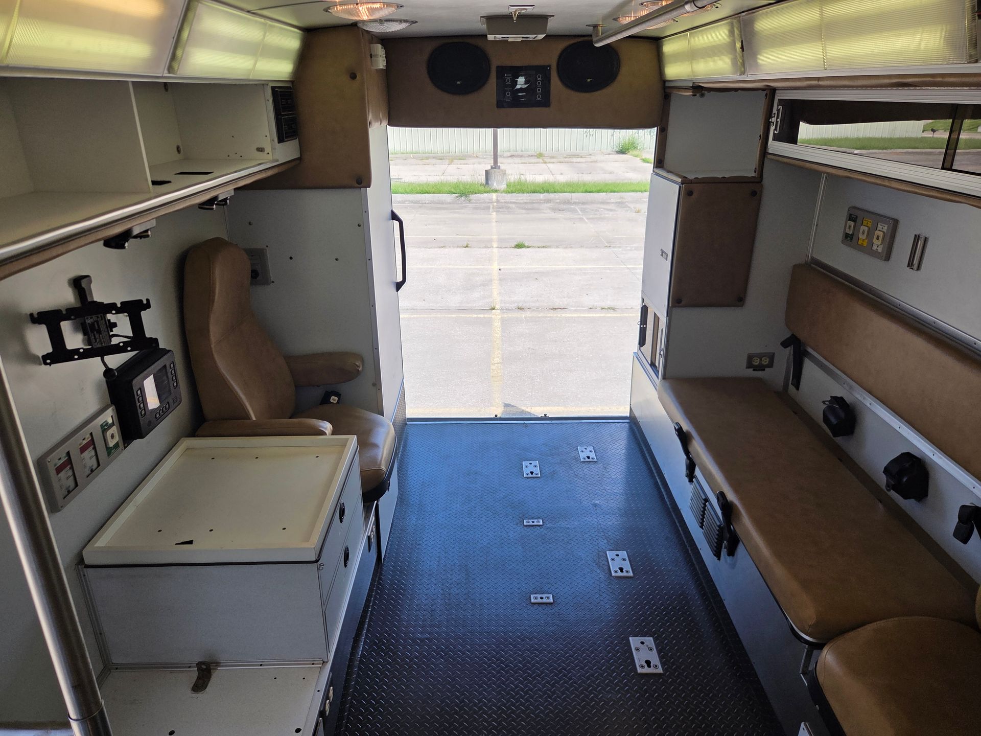 Interior of a small camper van with open rear doors, benches, cabinets, and a ribbed floor.