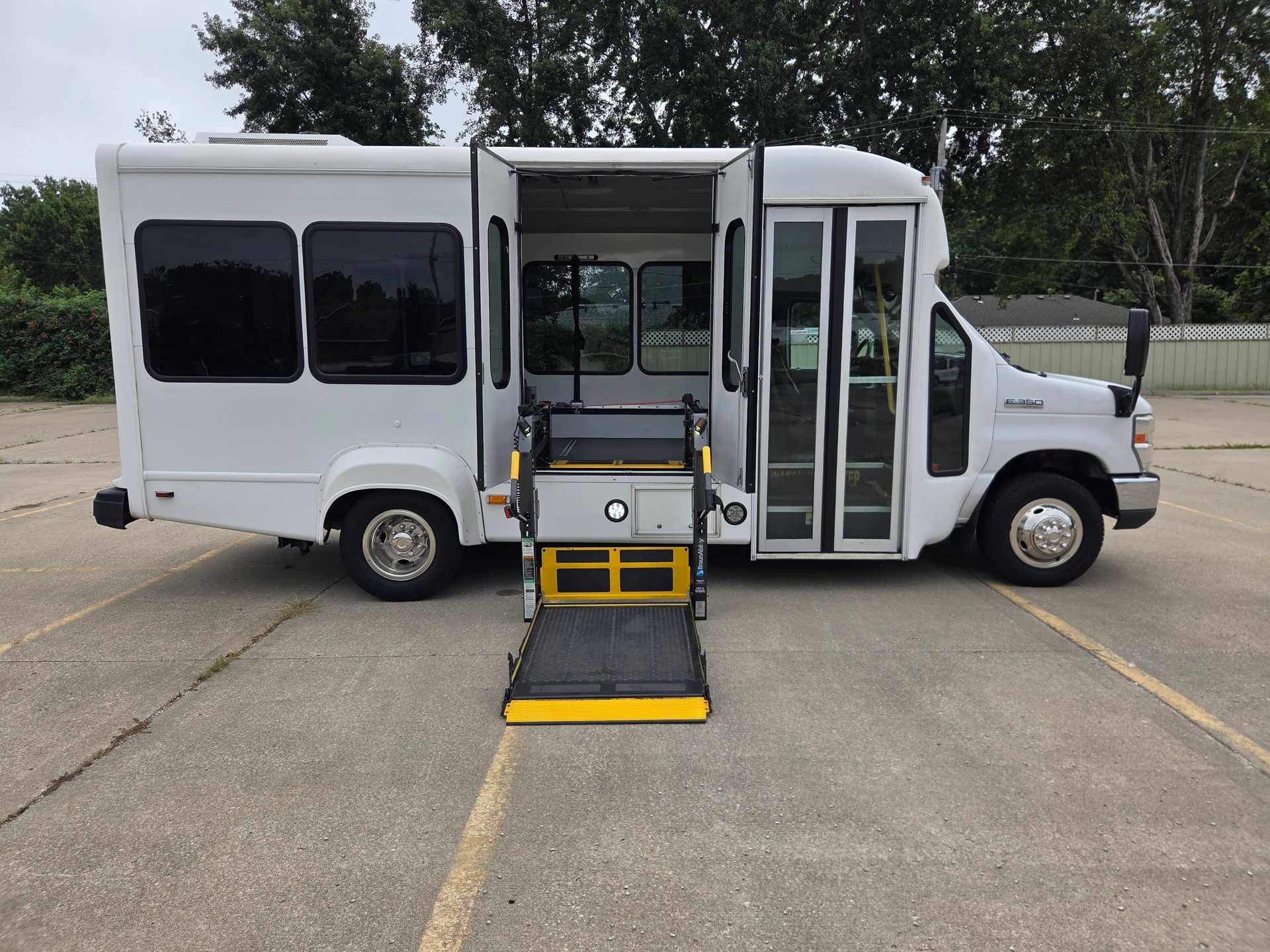 White shuttle bus with wheelchair lift ramp deployed on a parking lot roadway