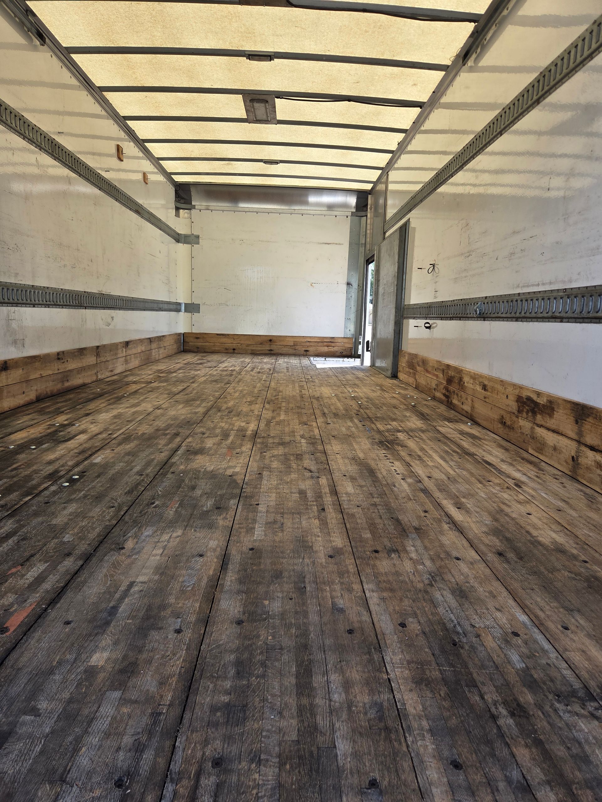 Empty cargo truck interior with worn wooden floor and white walls