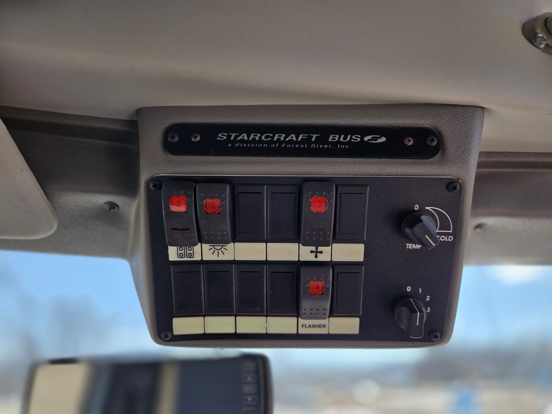 Overhead vehicle control panel with red-lit switches and dials mounted near the windshield