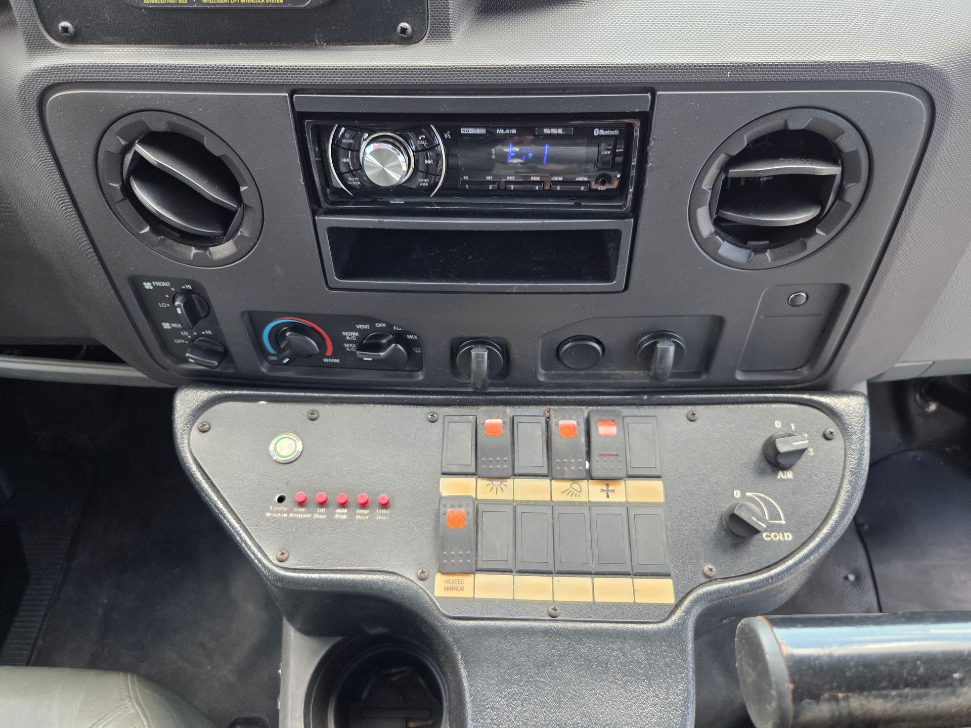Vehicle dashboard with radio and climate controls above a custom control panel with switches and knobs