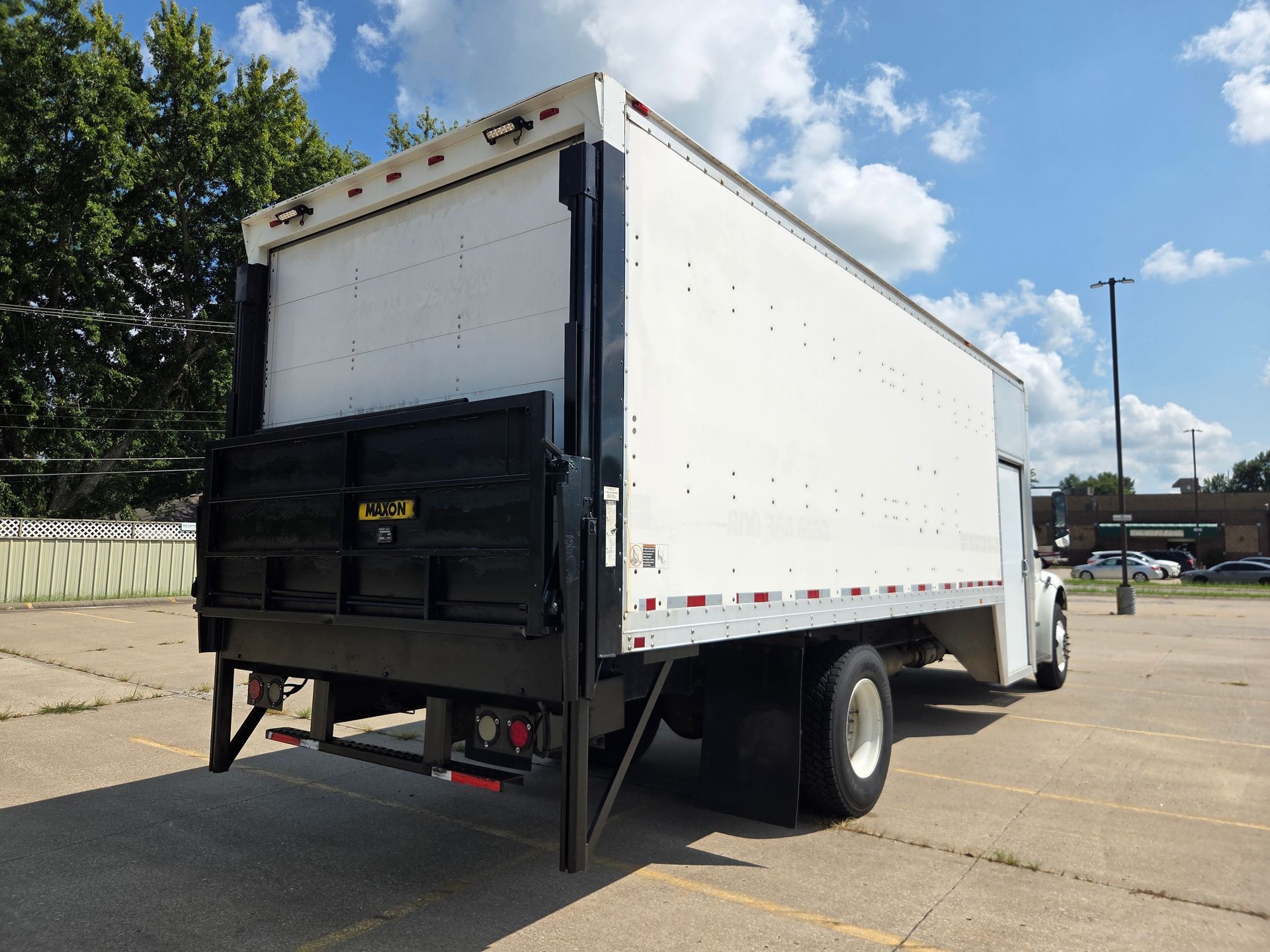 White box truck parked on a sunny street, rear view with black tailgate and metal ramp.