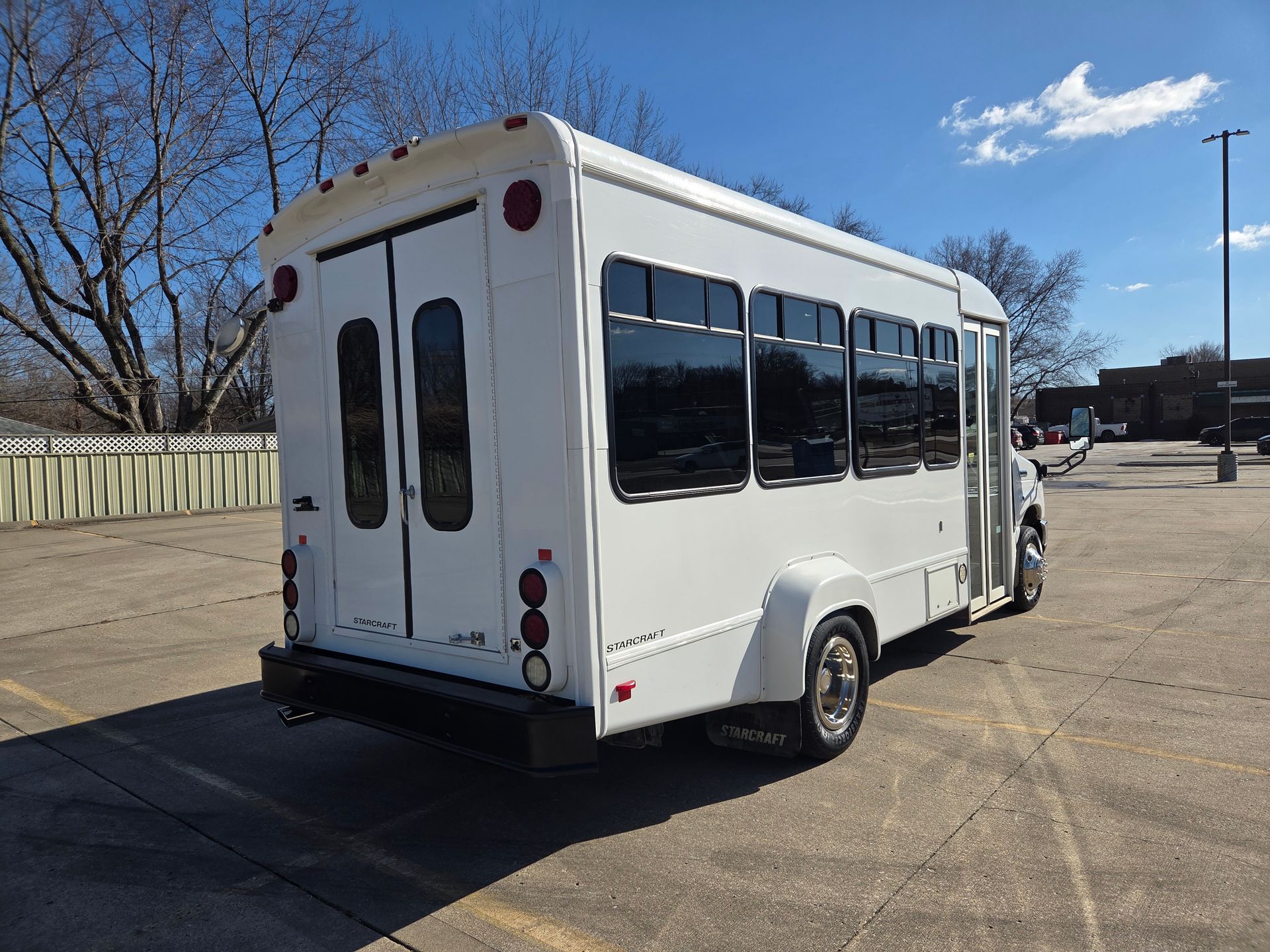 White shuttle bus parked in a lot, rear view with tinted windows and red taillights under a blue sky