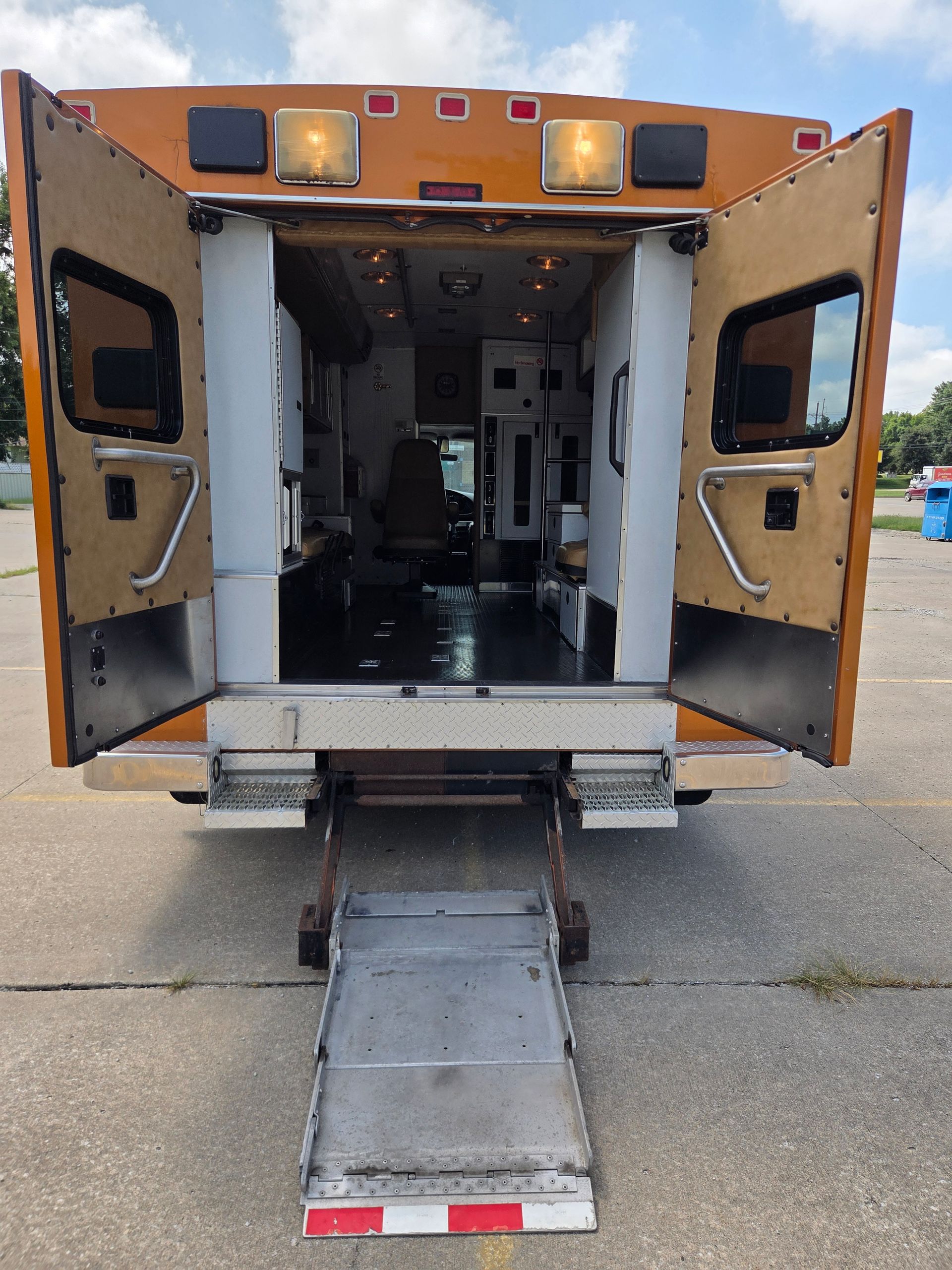 Ambulance with rear doors open and a folded loading ramp extended to the pavement