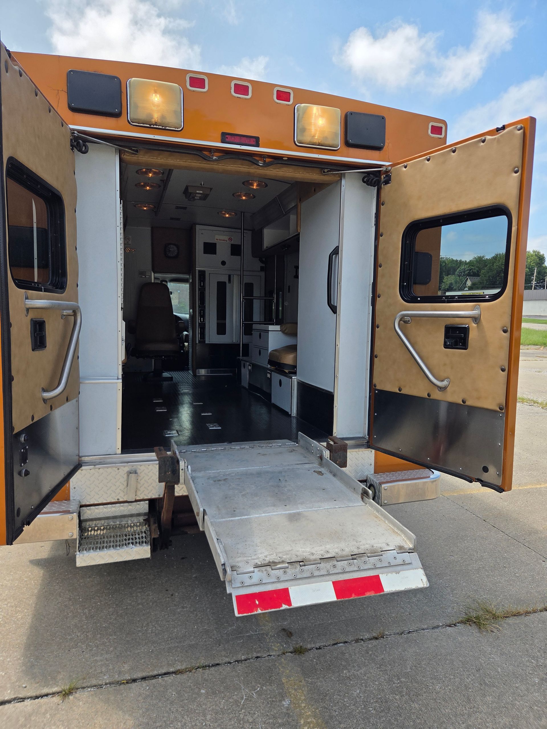 Open rear doors of an ambulance with a ramp lowered to the pavement.
