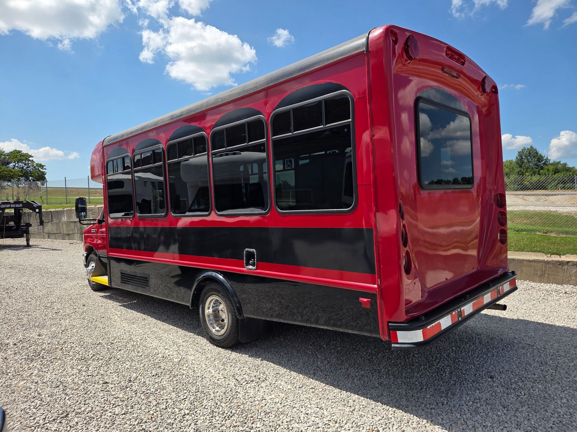 Red and black shuttle bus parked on a gravel lot under a blue sky