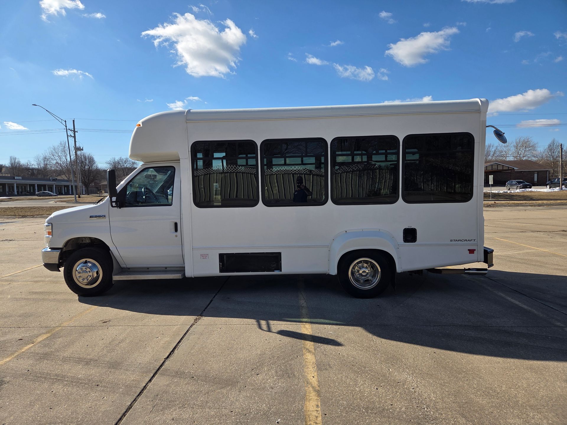 White shuttle bus parked on a sunny paved lot under a blue sky