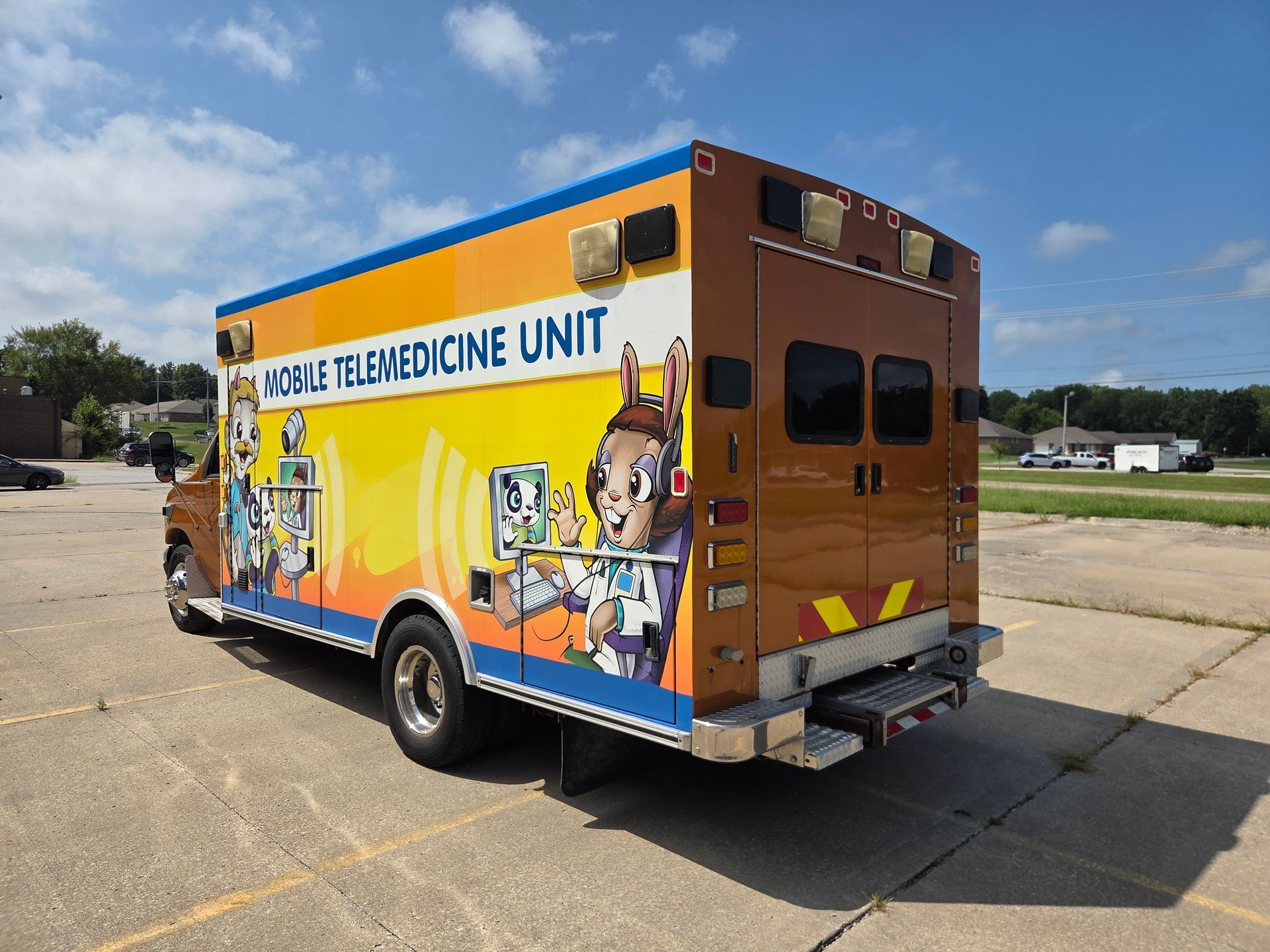 Orange mobile telemedicine unit van parked on a sunny lot, with colorful medical graphics on the side