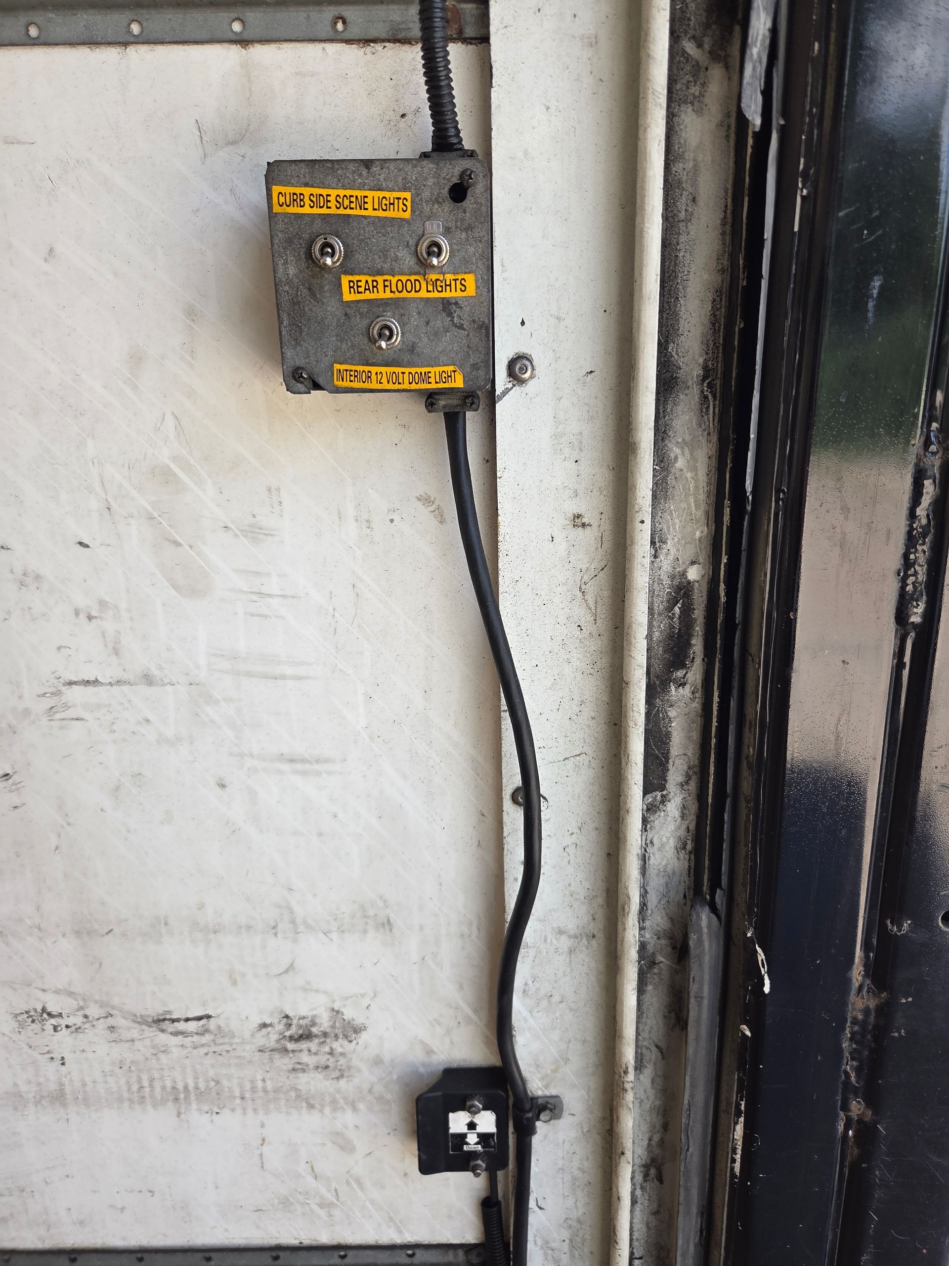 Electrical control box and wiring mounted on a dirty white wall beside a black door frame.