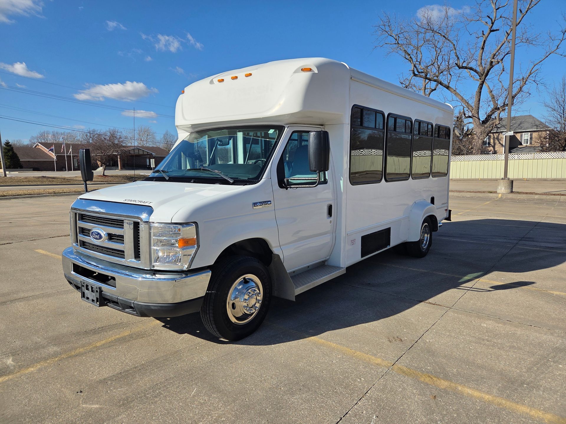 White shuttle bus parked on a paved lot under a clear blue sky