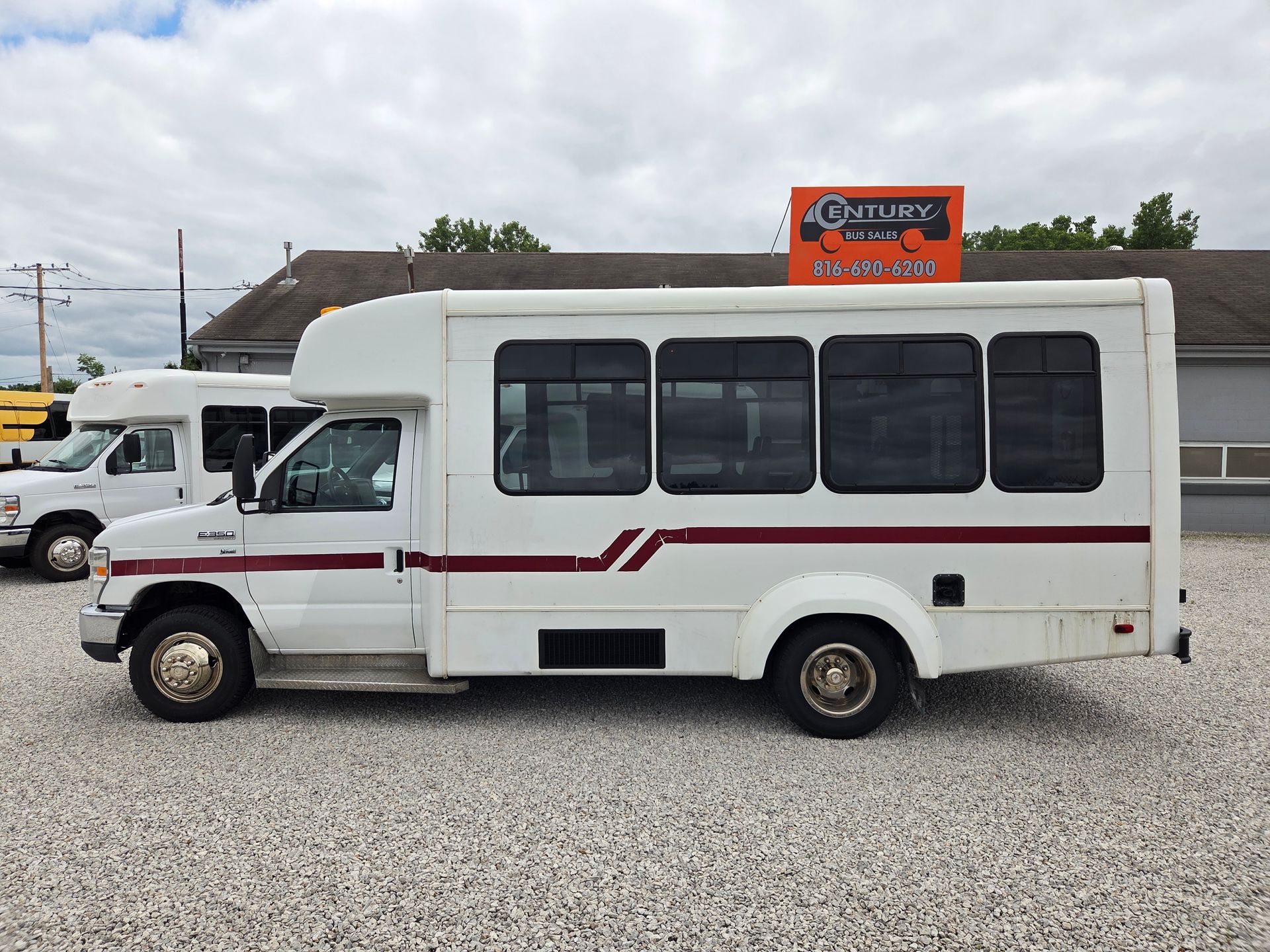 White passenger shuttle van parked on gravel lot with red stripe and orange sign in background