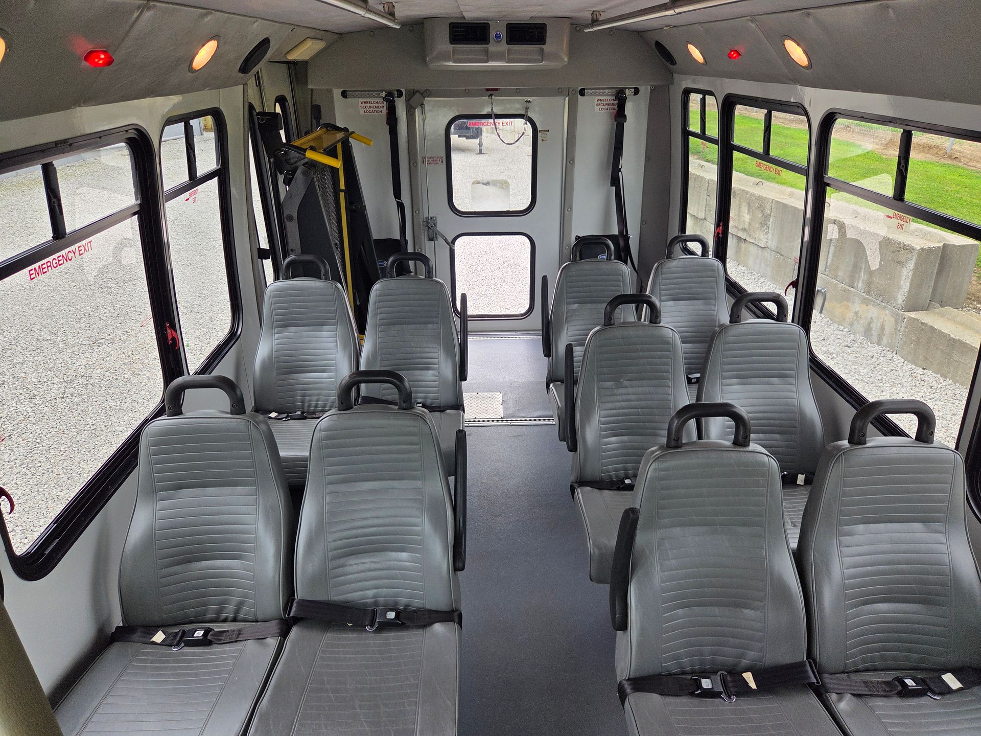 Empty bus interior with gray seats and large windows, viewed from the rear toward the front door.