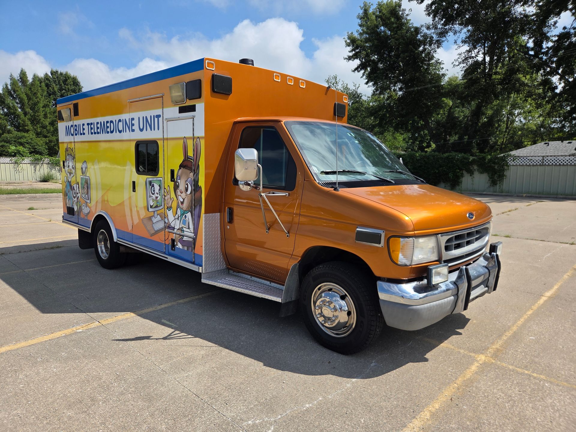 Orange food truck parked in a sunny lot, with blue and yellow service side graphics