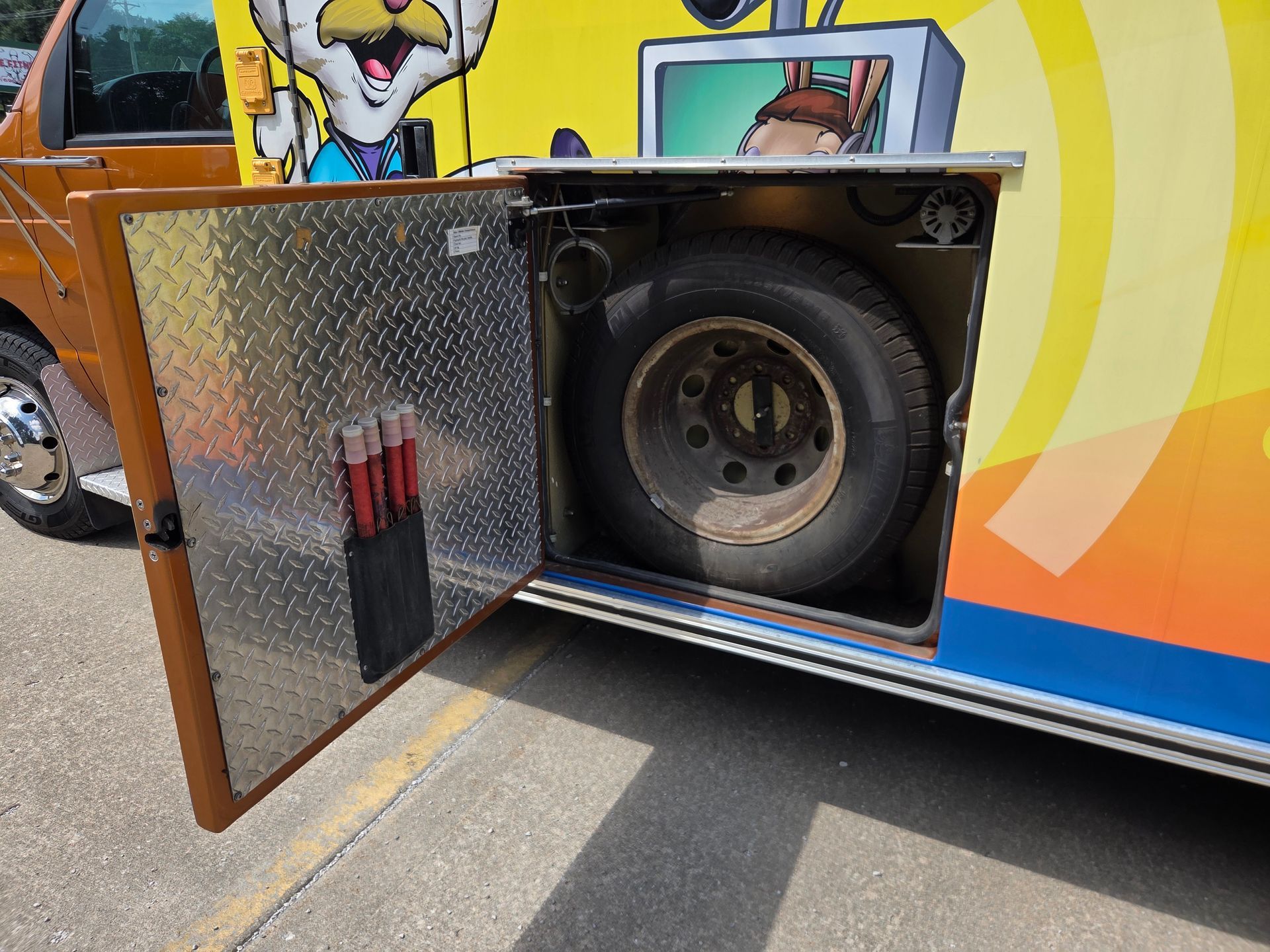 Open compartment on colorful truck revealing a spare tire and tools inside