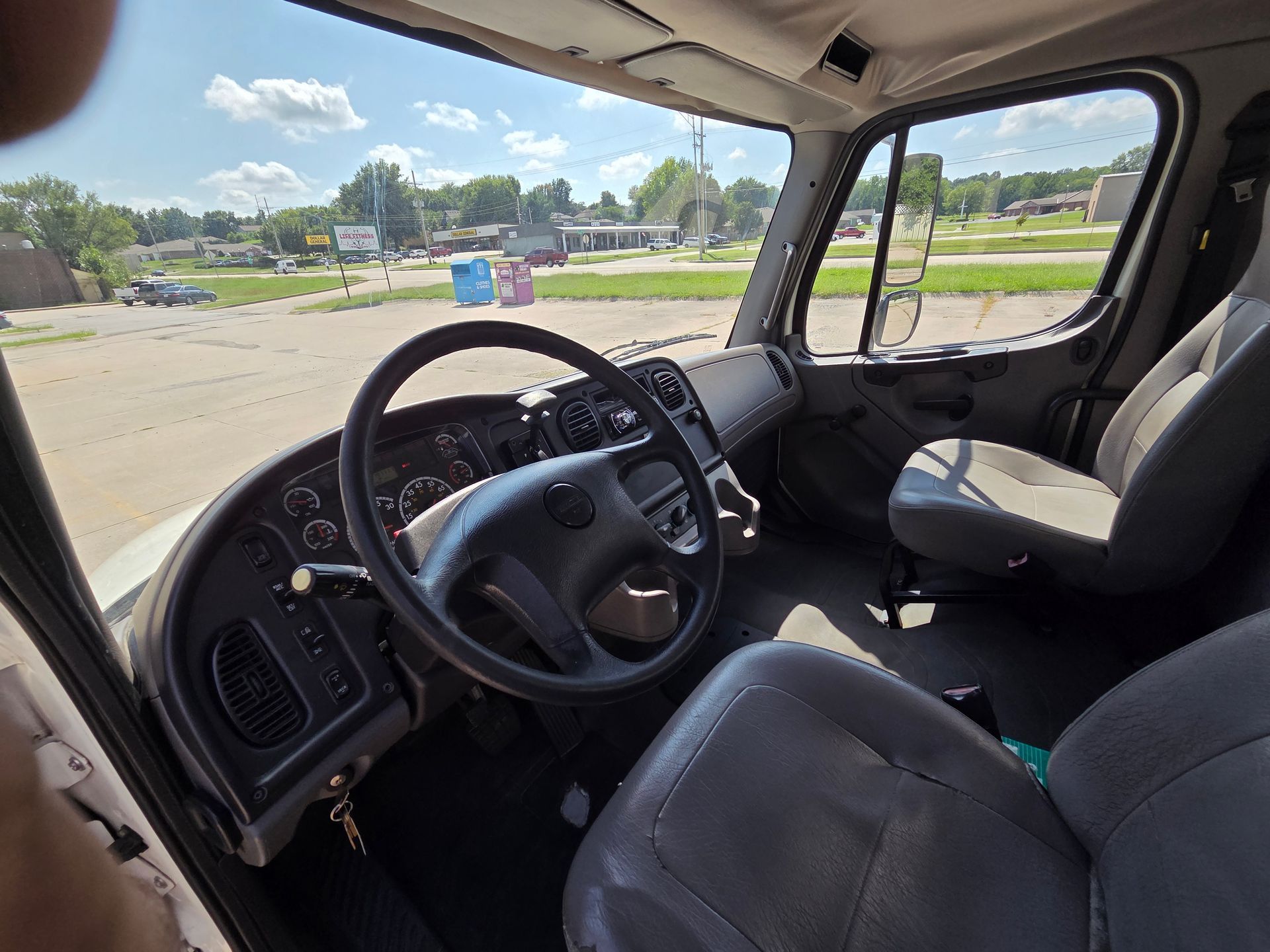 Pickup truck interior with steering wheel and front seats, parked in an open lot.