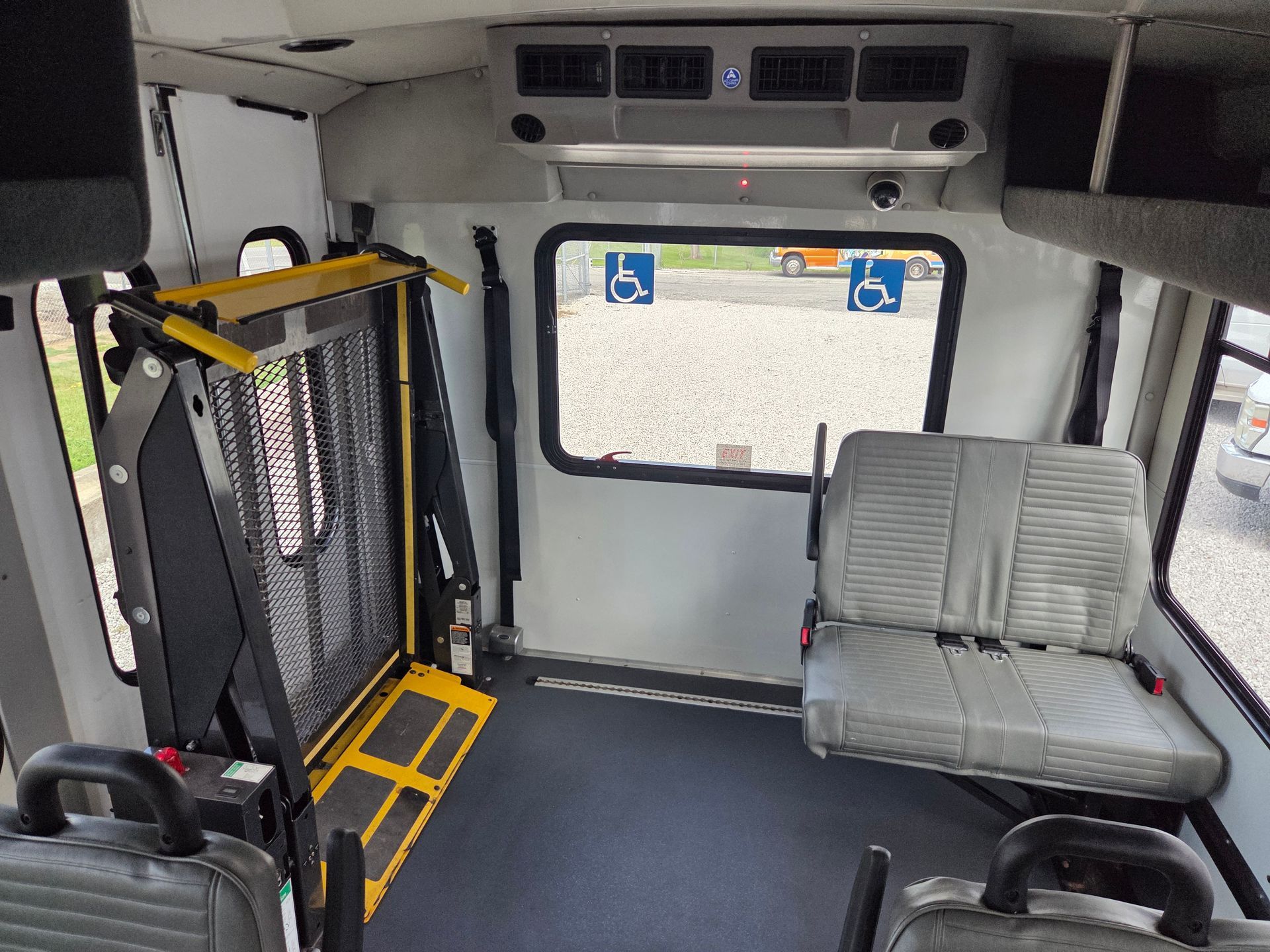 Interior of an accessible van with a wheelchair lift, folding seat, and gray carpeted floor.