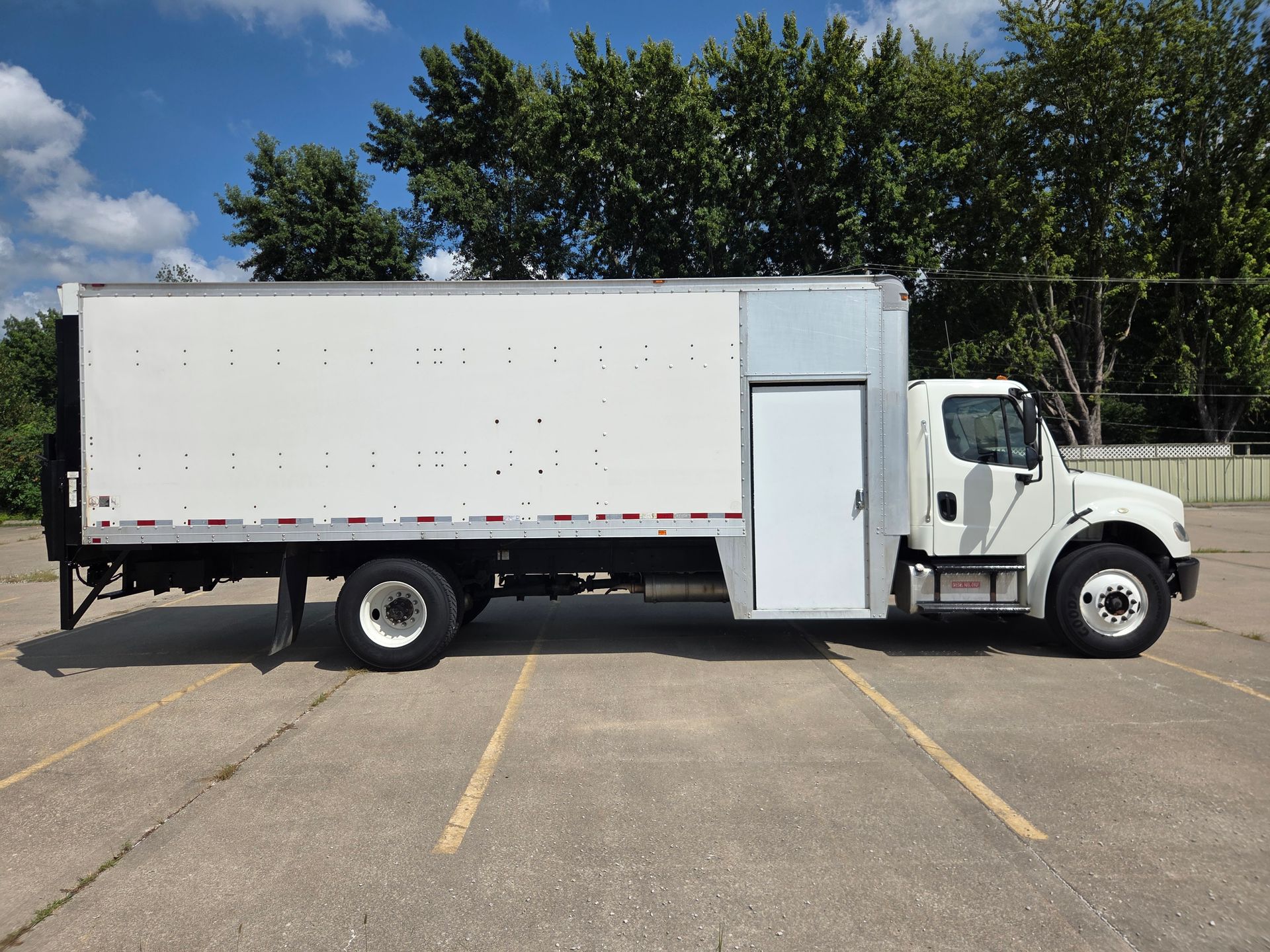 White box truck parked in an empty lot with trees in the background