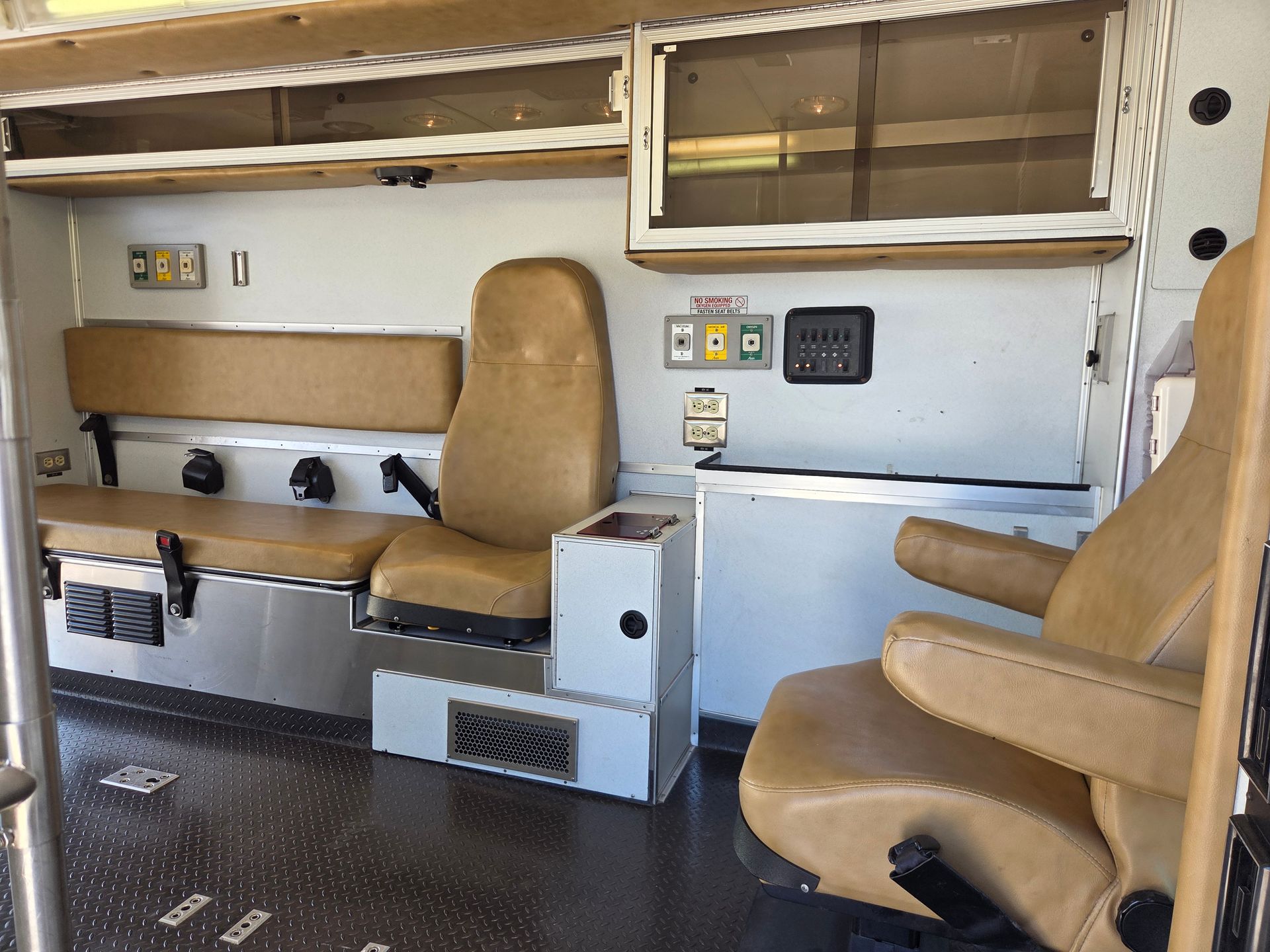 Interior of a utility vehicle with tan jump seats and storage shelves, showing a compact workspace area