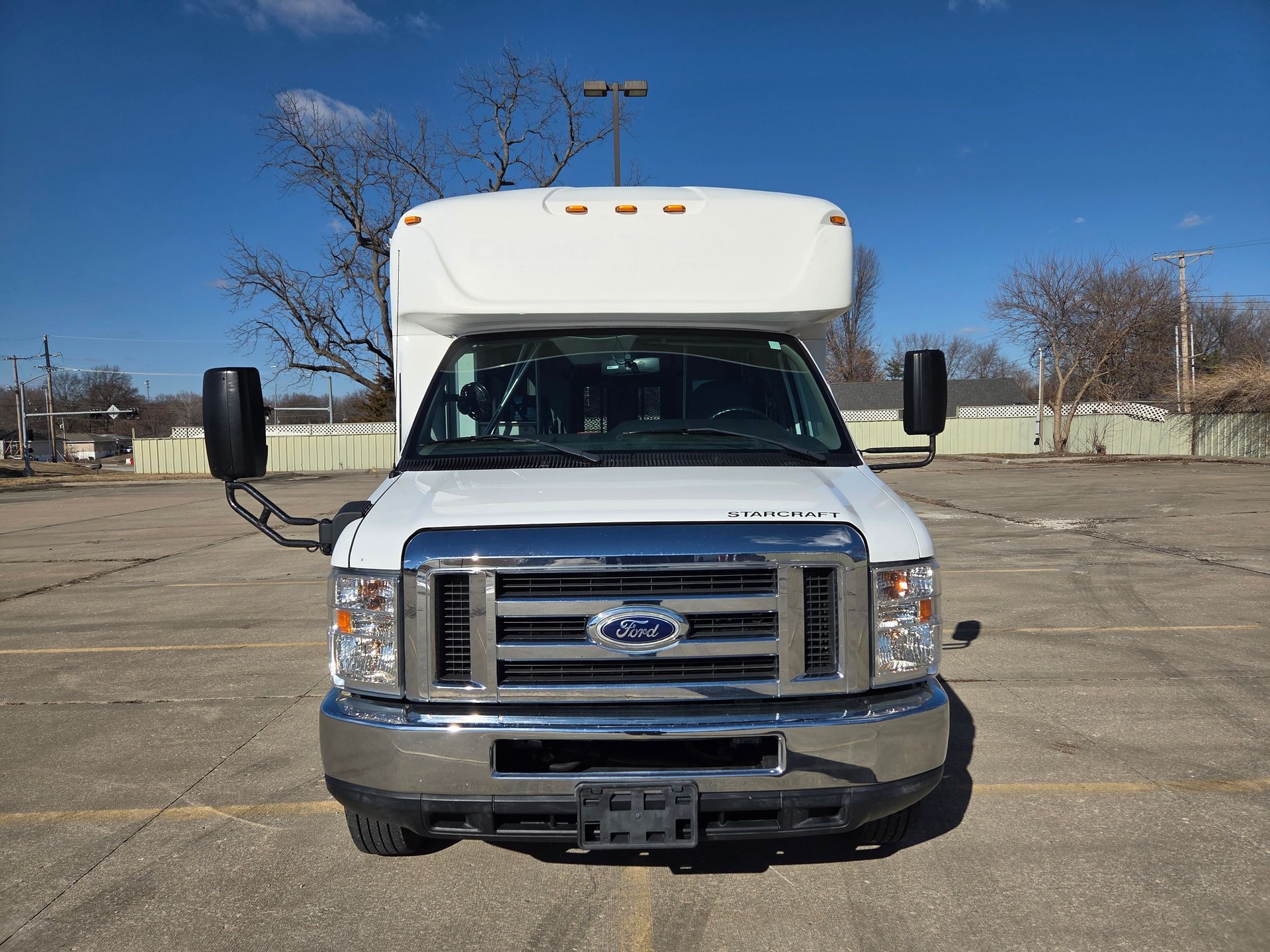 Front view of a white Ford shuttle bus parked in an empty lot under a blue sky.