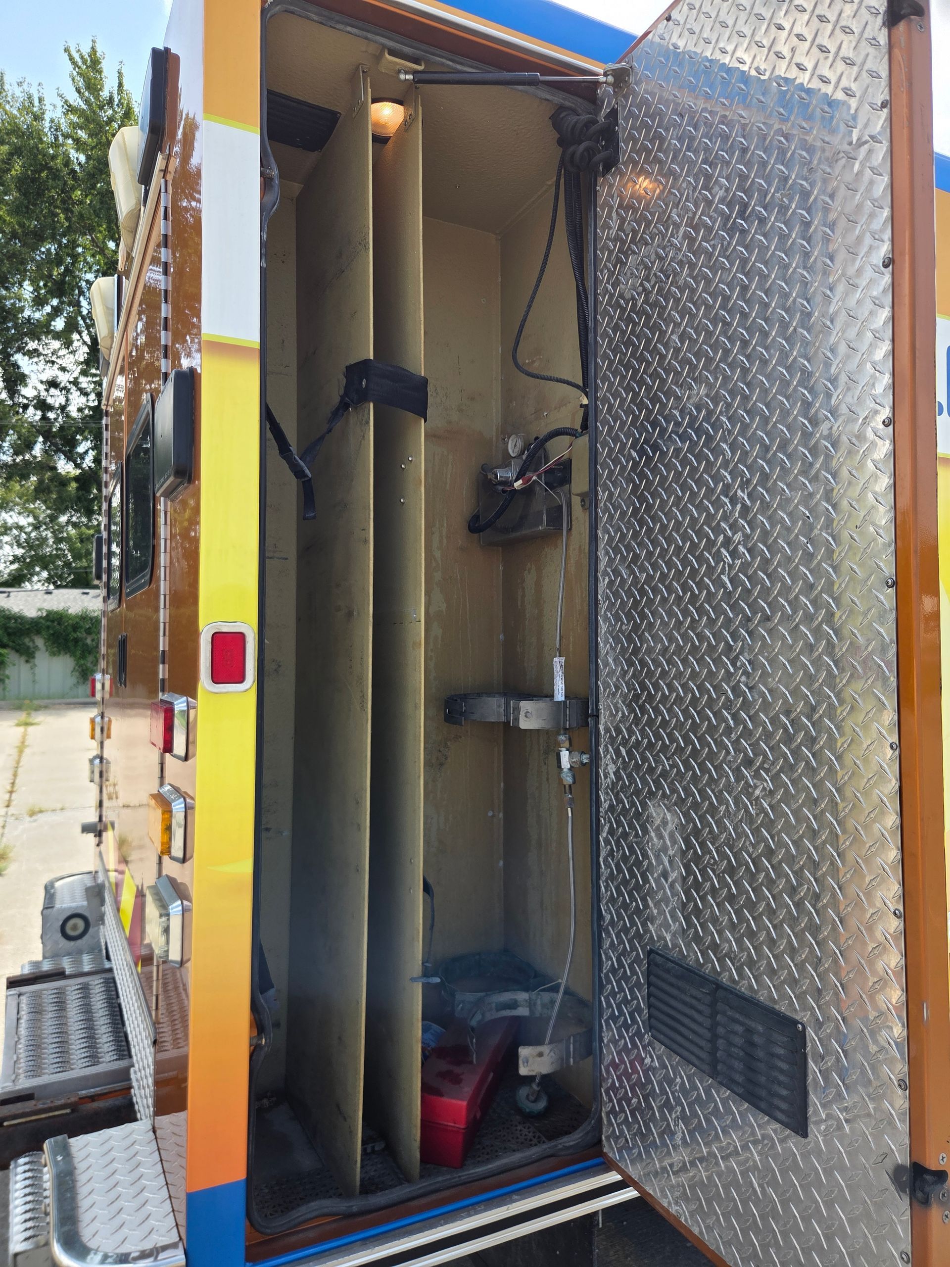 Open utility cabinet with hoses, pipes, and tools inside a yellow work vehicle.