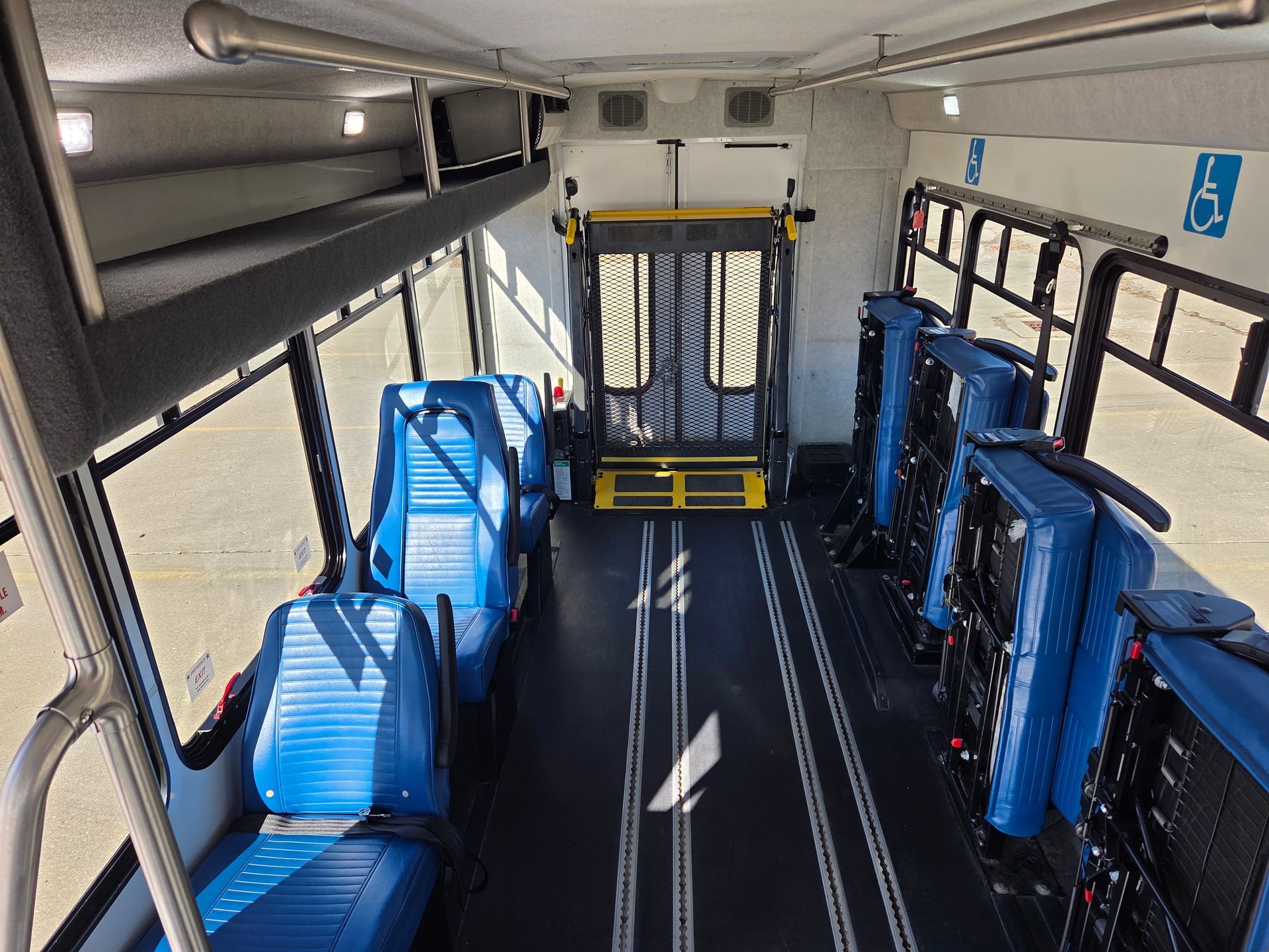 Empty bus interior with blue seats and wheelchair-accessible space near the front and rear doors