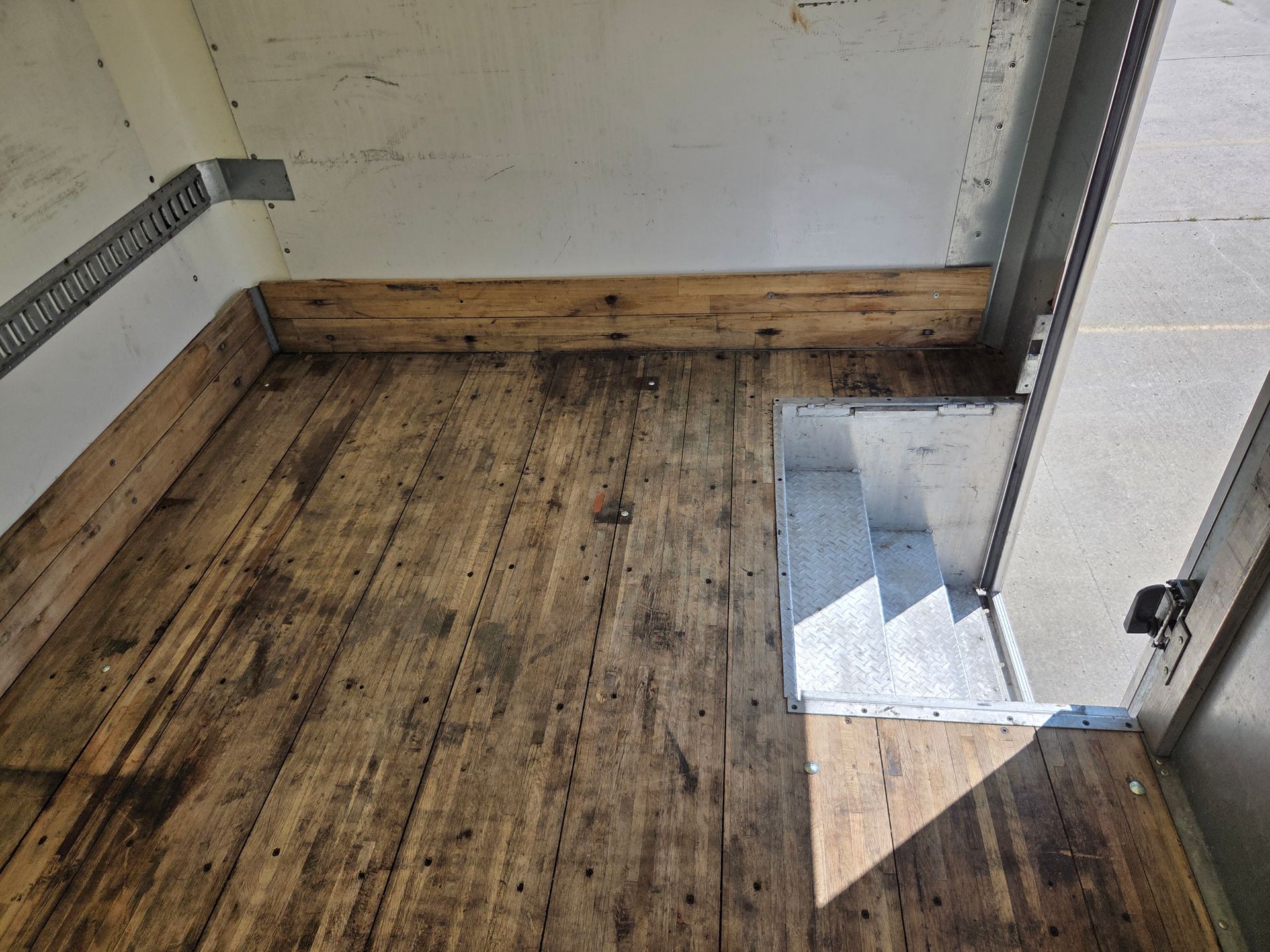 Empty wooden floor in a small unfinished room with a sunlit doorway and tiled step.