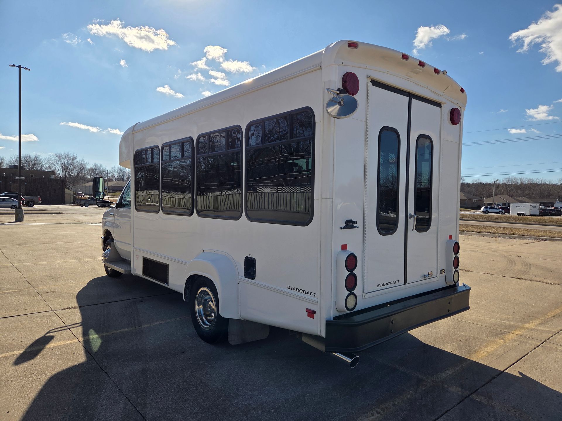 White shuttle bus parked in a lot under a blue sky, rear and side view