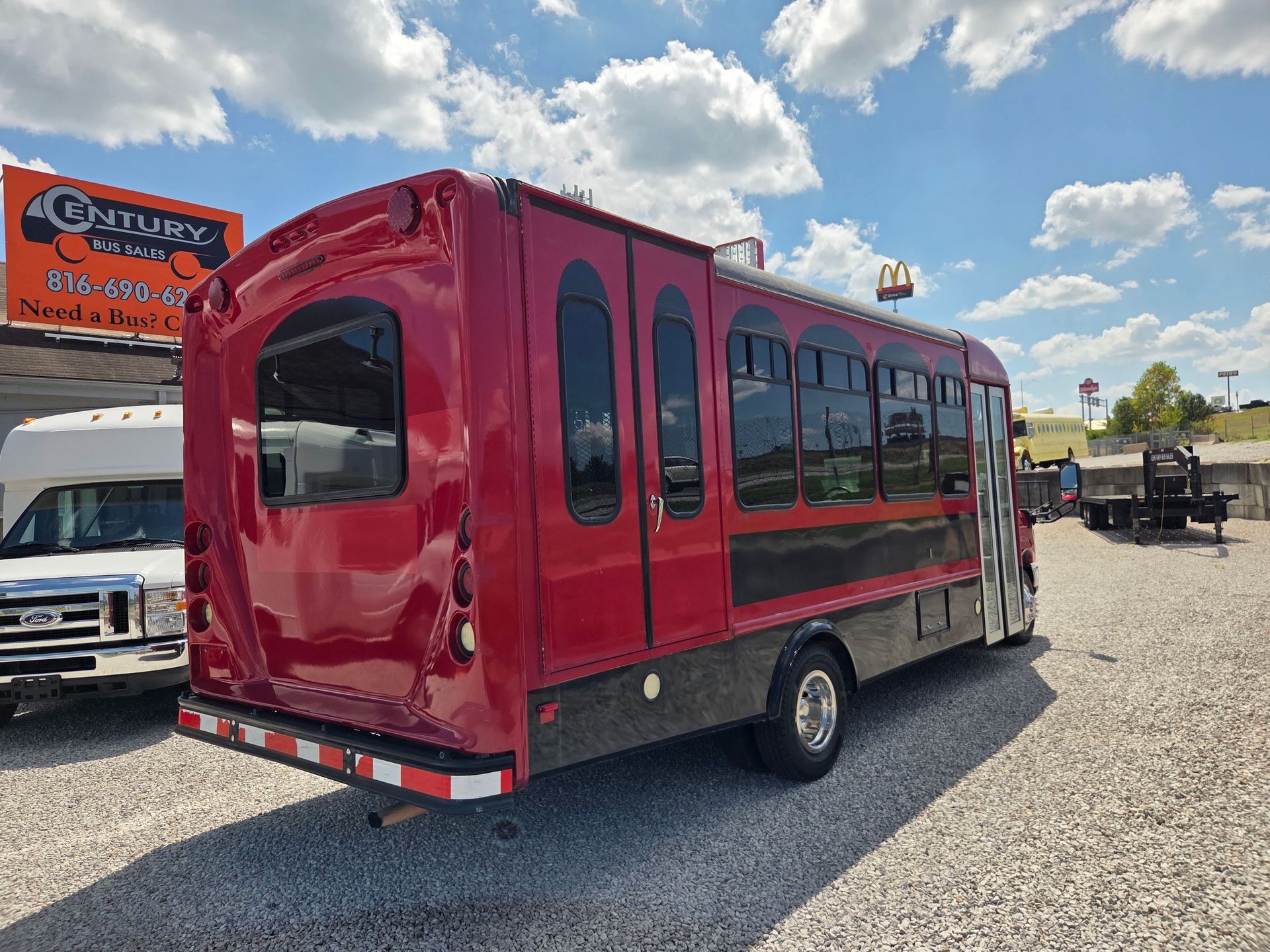 Red enclosed shuttle bus parked on gravel lot under a blue sky