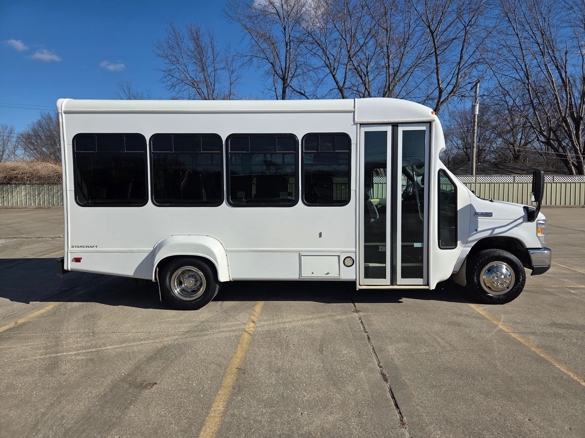 White shuttle bus parked on an empty lot under a blue sky