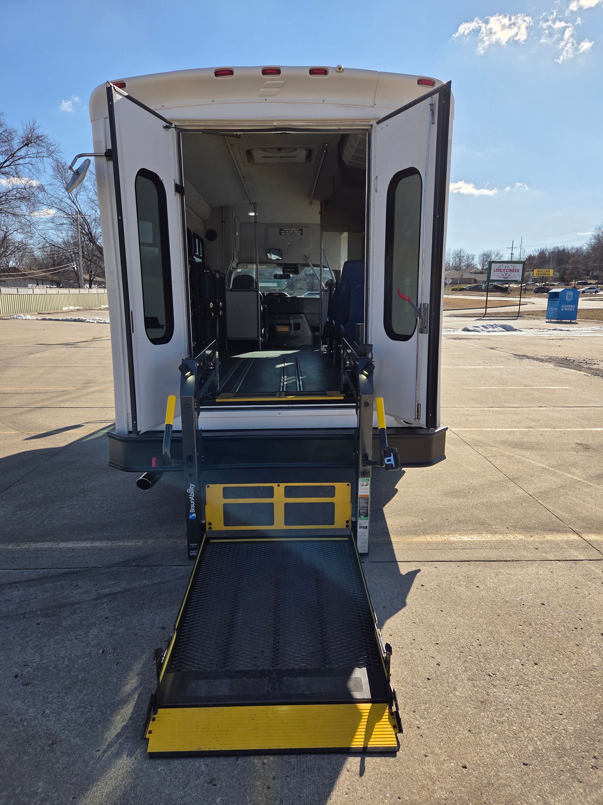 Rear view of a white wheelchair-accessible van with its lift ramp extended in a parking lot.