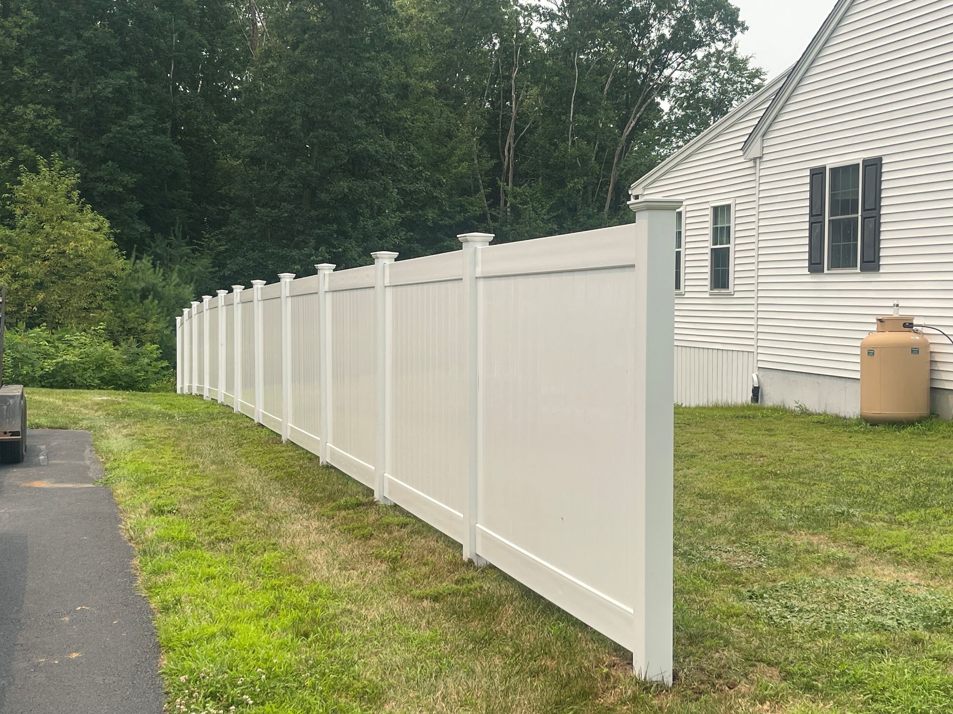 Long white vinyl privacy fence beside a house along a grassy yard and driveway